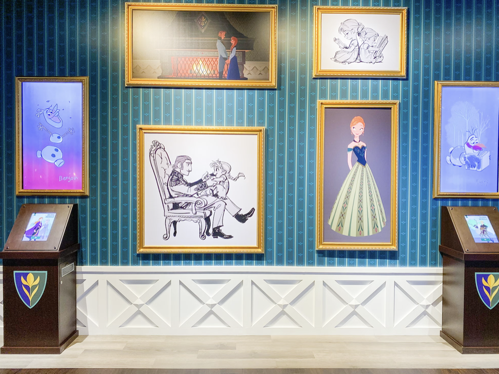 Wall decorated with digital art and sketches from Disney's Frozen, featuring characters like Olaf, Anna, and Elsa, with interactive screens on both sides.