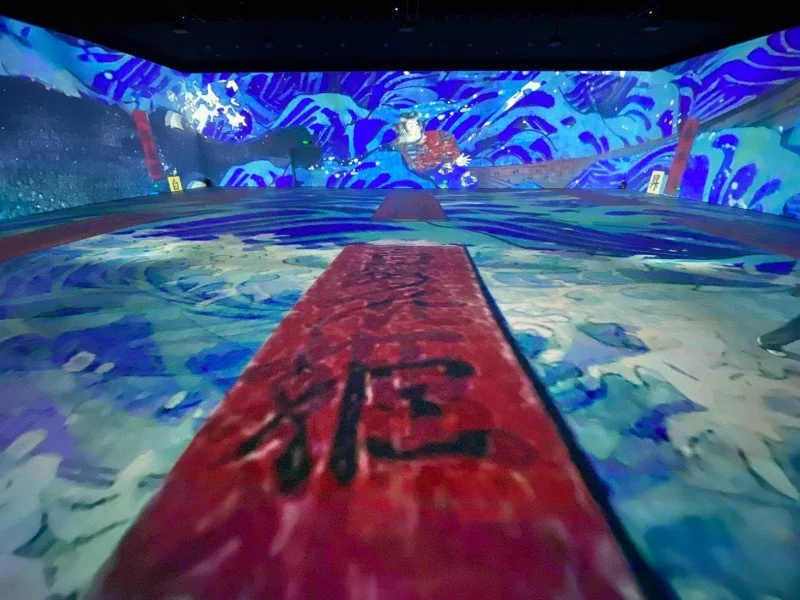 Indoor mini-golf course with colorful, ocean-themed murals on walls and floor, featuring waves and water motifs