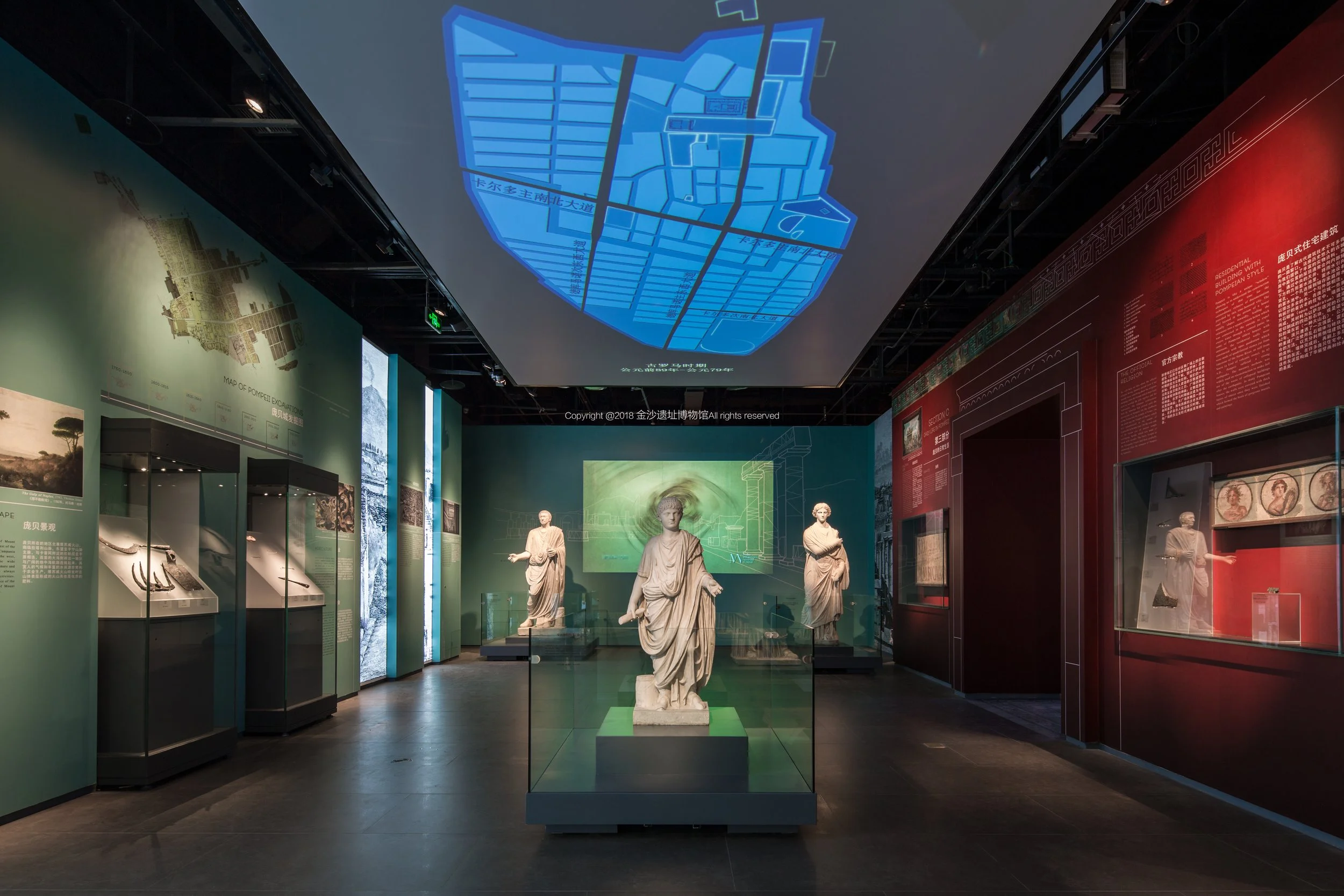 Interior of a museum with ancient statues on display and informational panels on the walls, with a blue map projection on the ceiling.