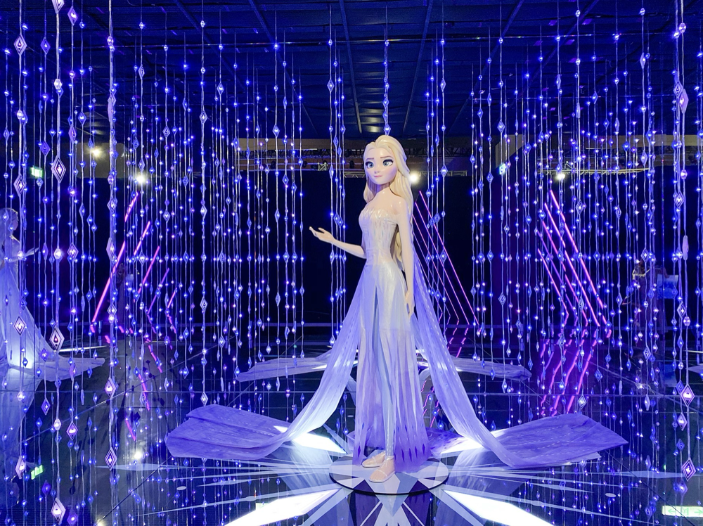 A Disney character from Frozen, Elsa, as a life-sized figure surrounded by blue and purple LED lights in a display.