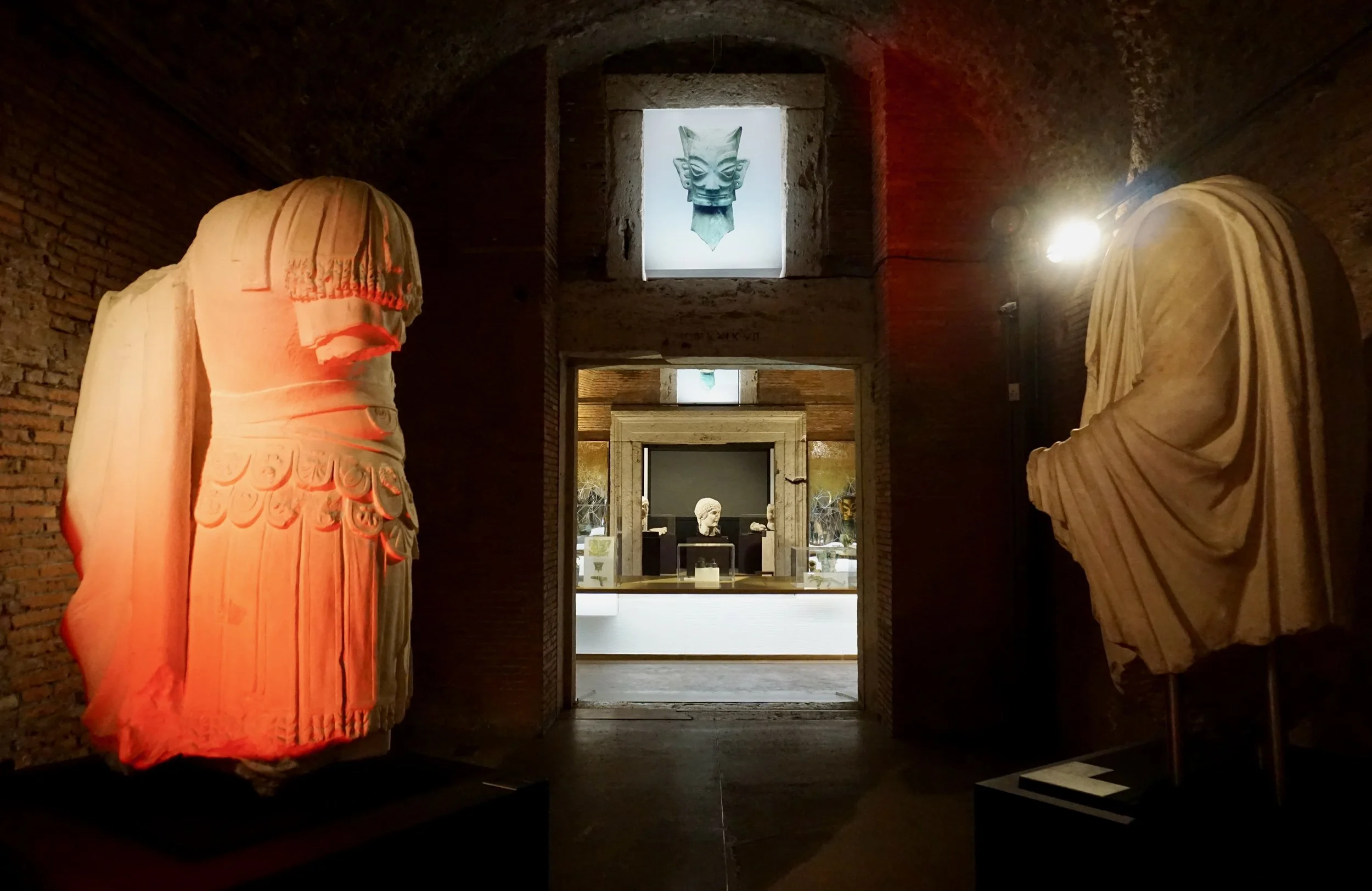 Museum exhibit with classical sculptures on display, illuminated with warm lighting inside a stone-walled room.