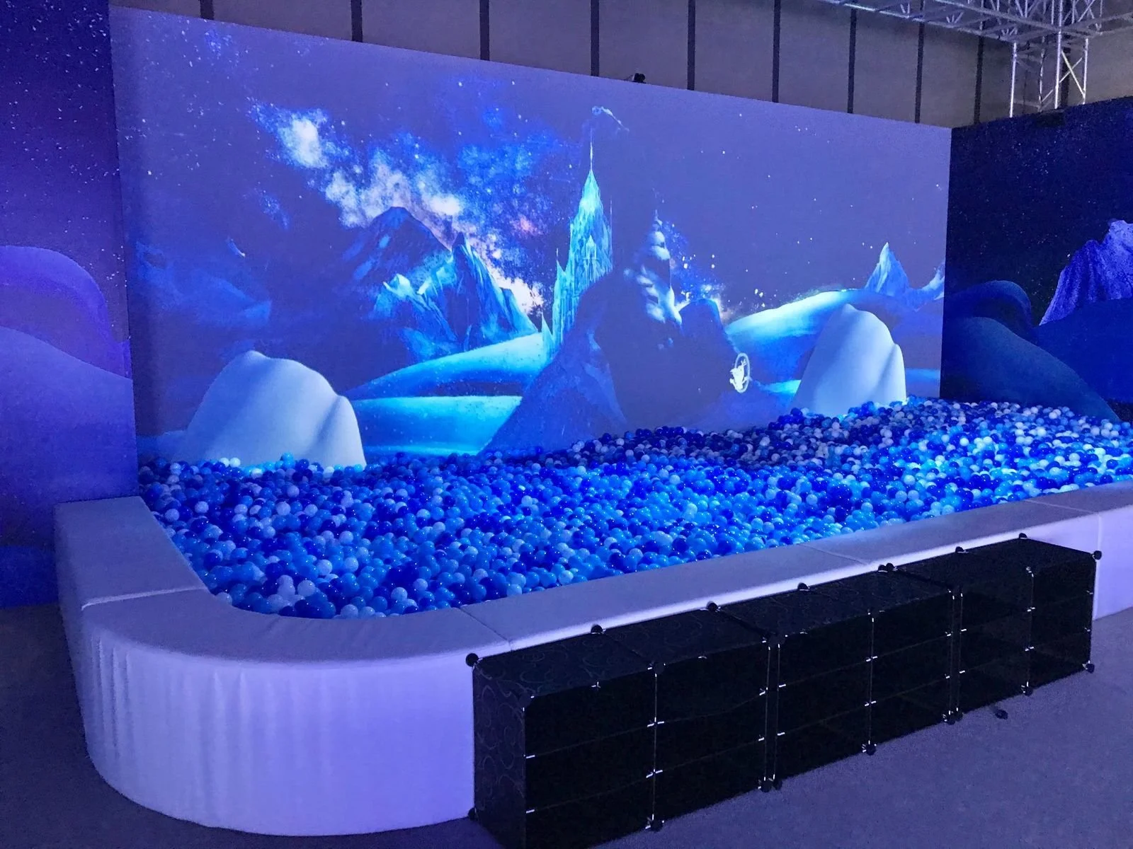 An interactive snow-themed display with a giant screen showing snowy mountains and night sky, filled with blue and white plastic balls resembling snow, and a low barrier around it.