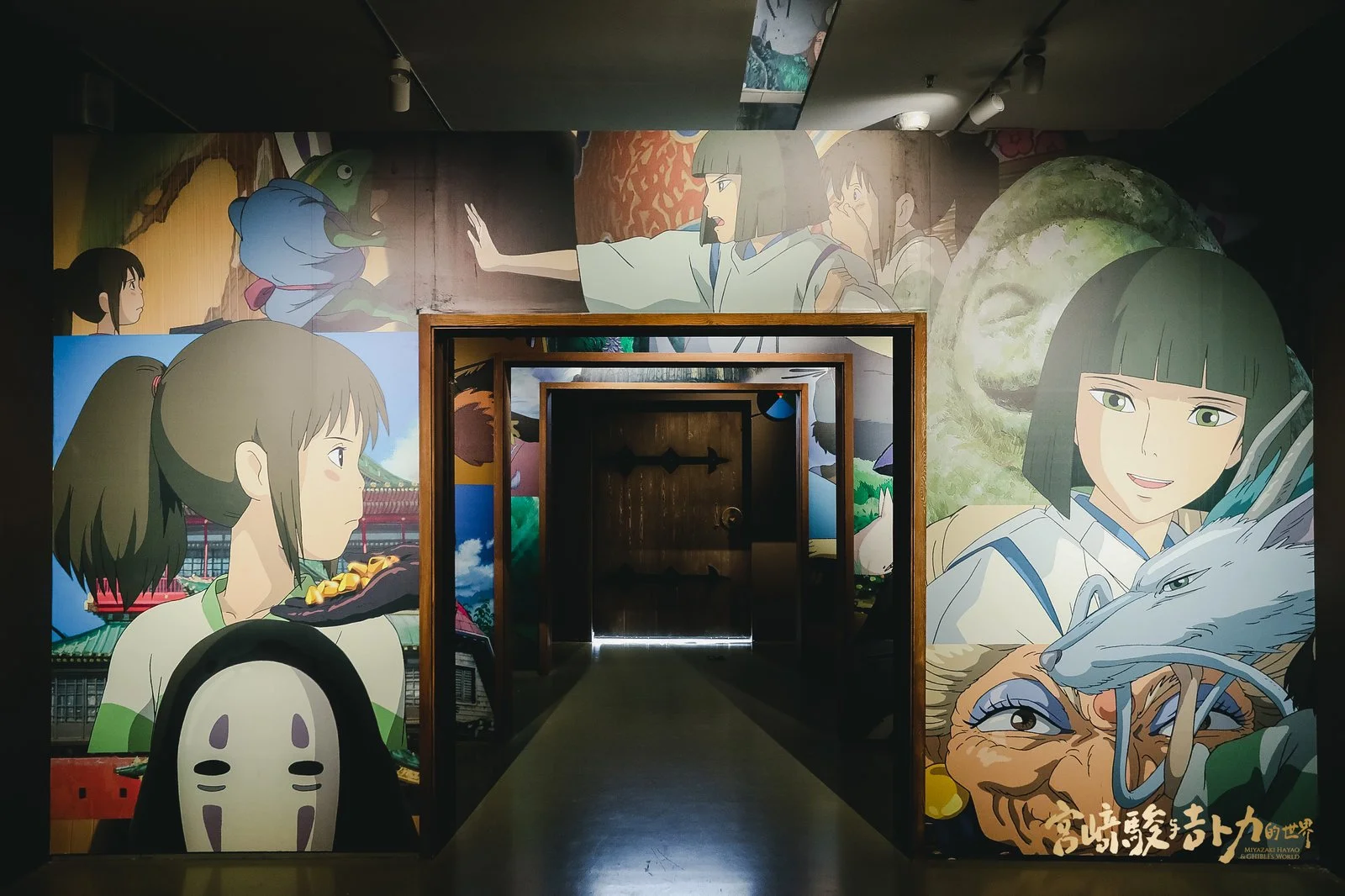 Colorful mural of characters from Studio Ghibli films, including princesses, creatures, and other figures, surrounds an entrance with a wooden door in the center.