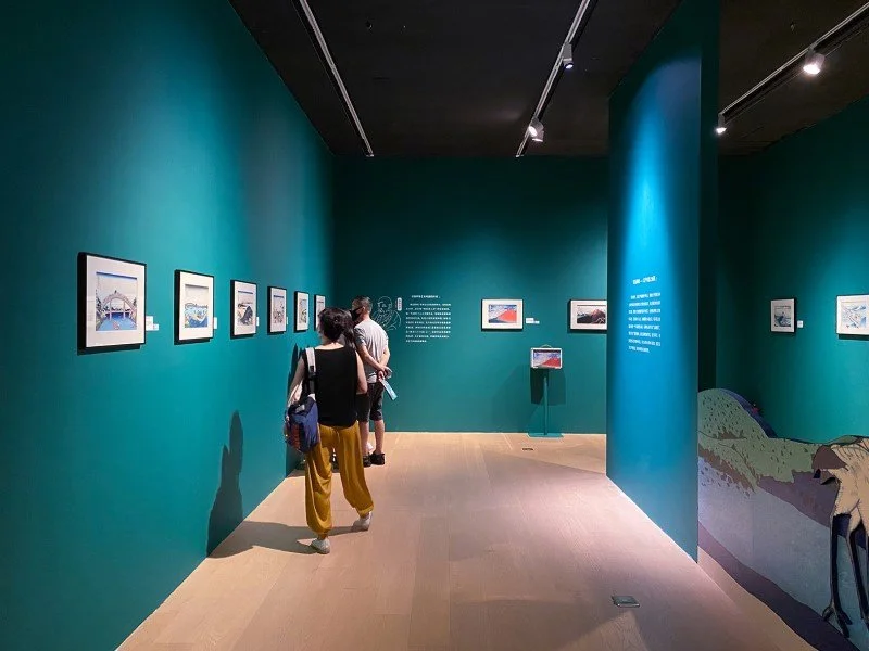 People viewing art on teal walls in an art gallery.