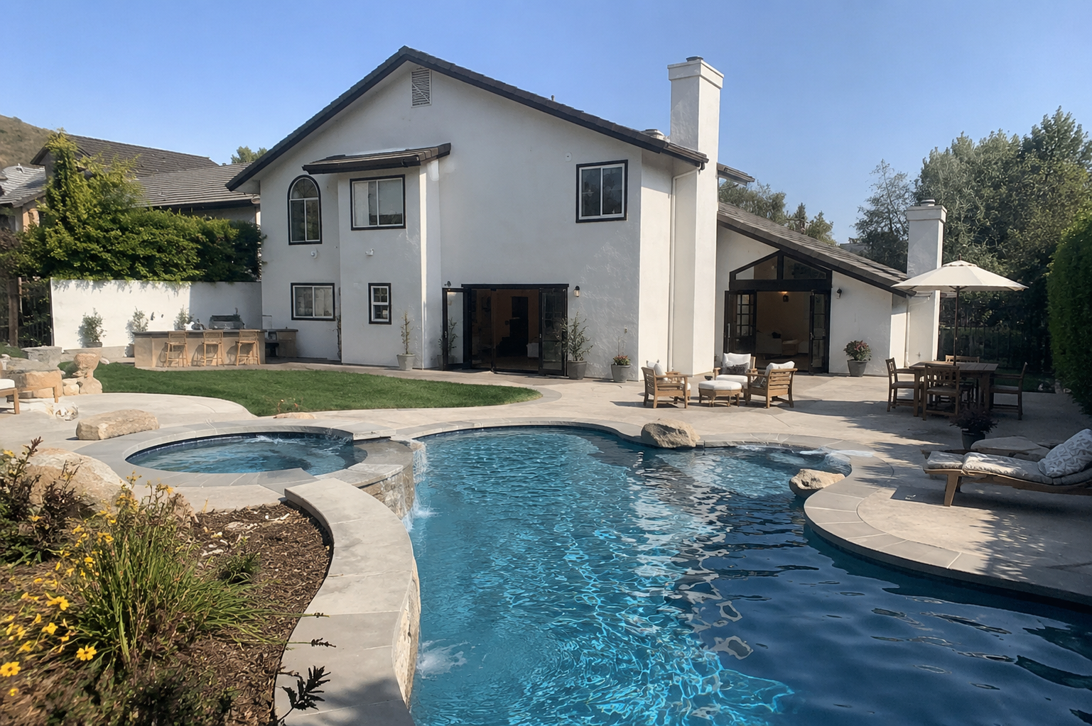 Backyard with swimming pool, hot tub, patio furniture, and a white house with black trim under a clear blue sky.