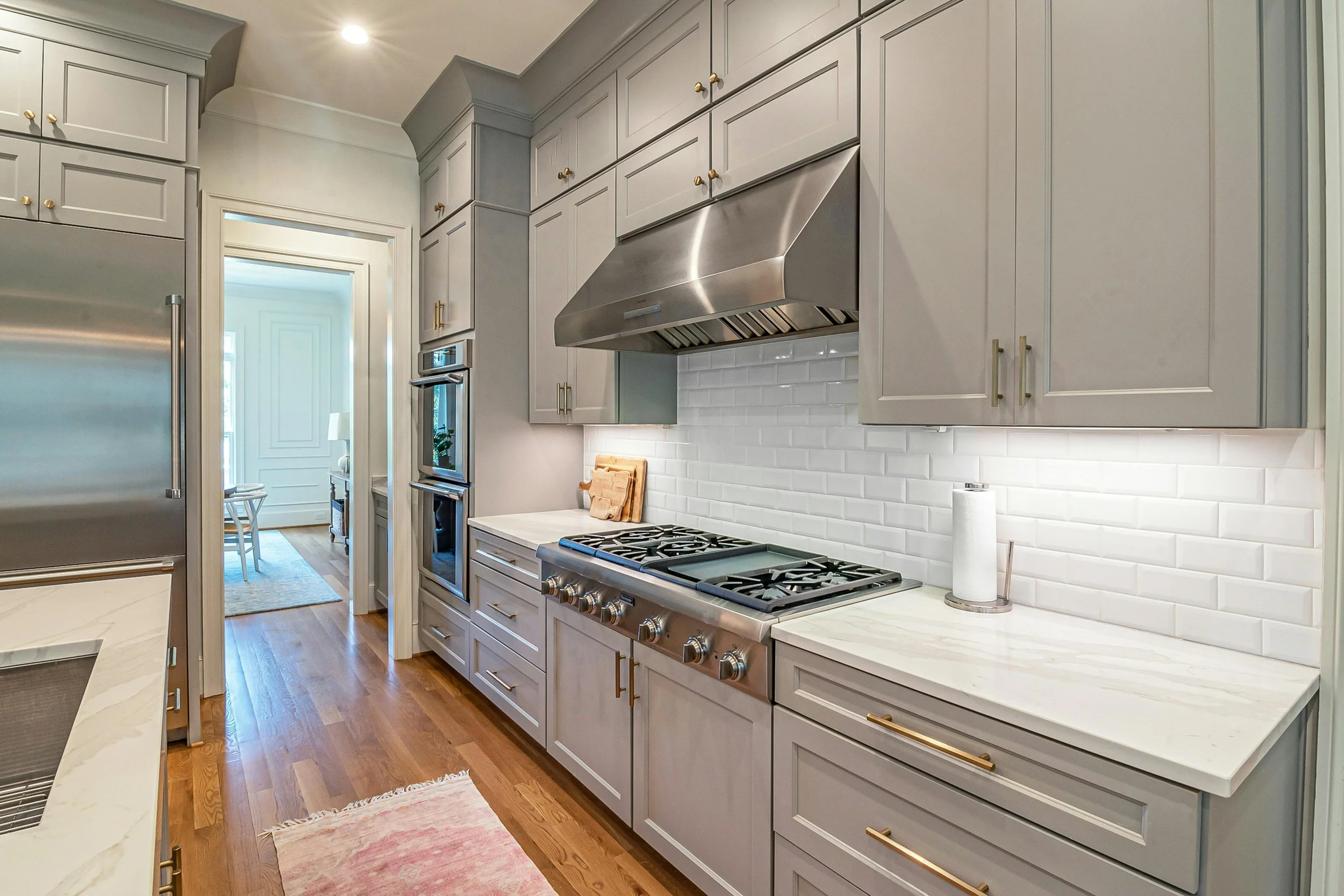 Modern kitchen with light gray cabinets, stainless steel range hood, white subway tile backsplash, stainless steel stove, and hardwood floors.