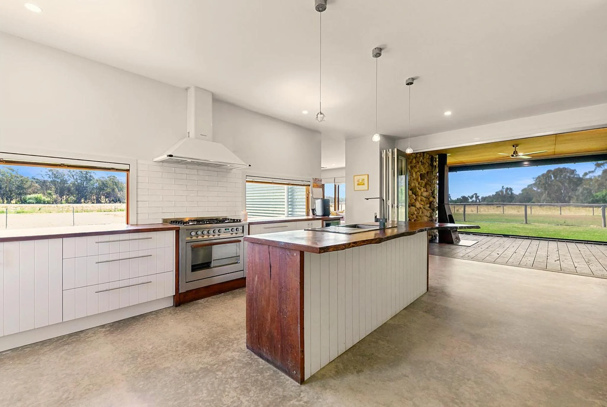 Modern open-plan kitchen with white cabinets, a wooden island, and large windows revealing a grassy outdoor area