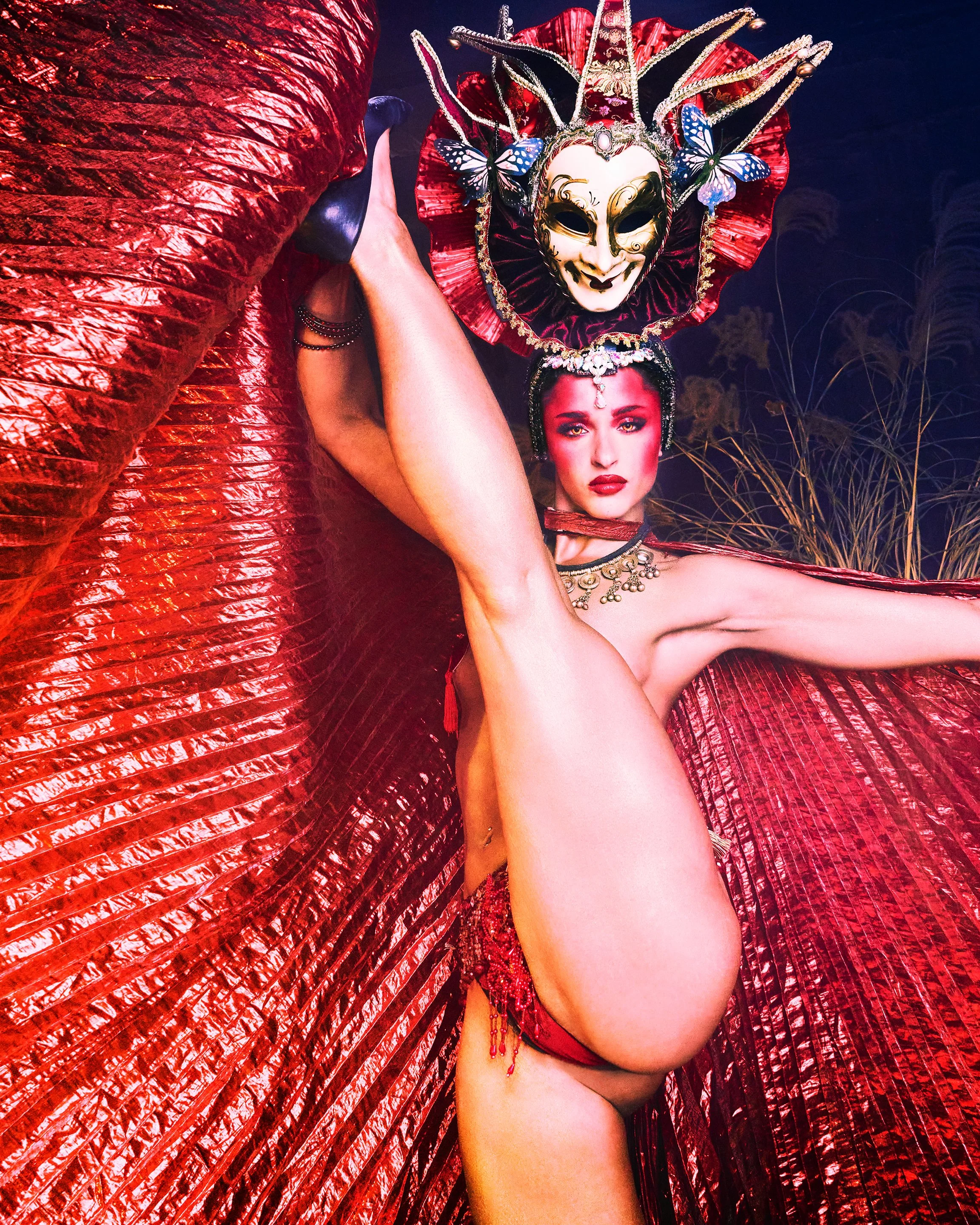 Person in elaborate red costume with large tutu and ornate mask, posing outdoors at night.