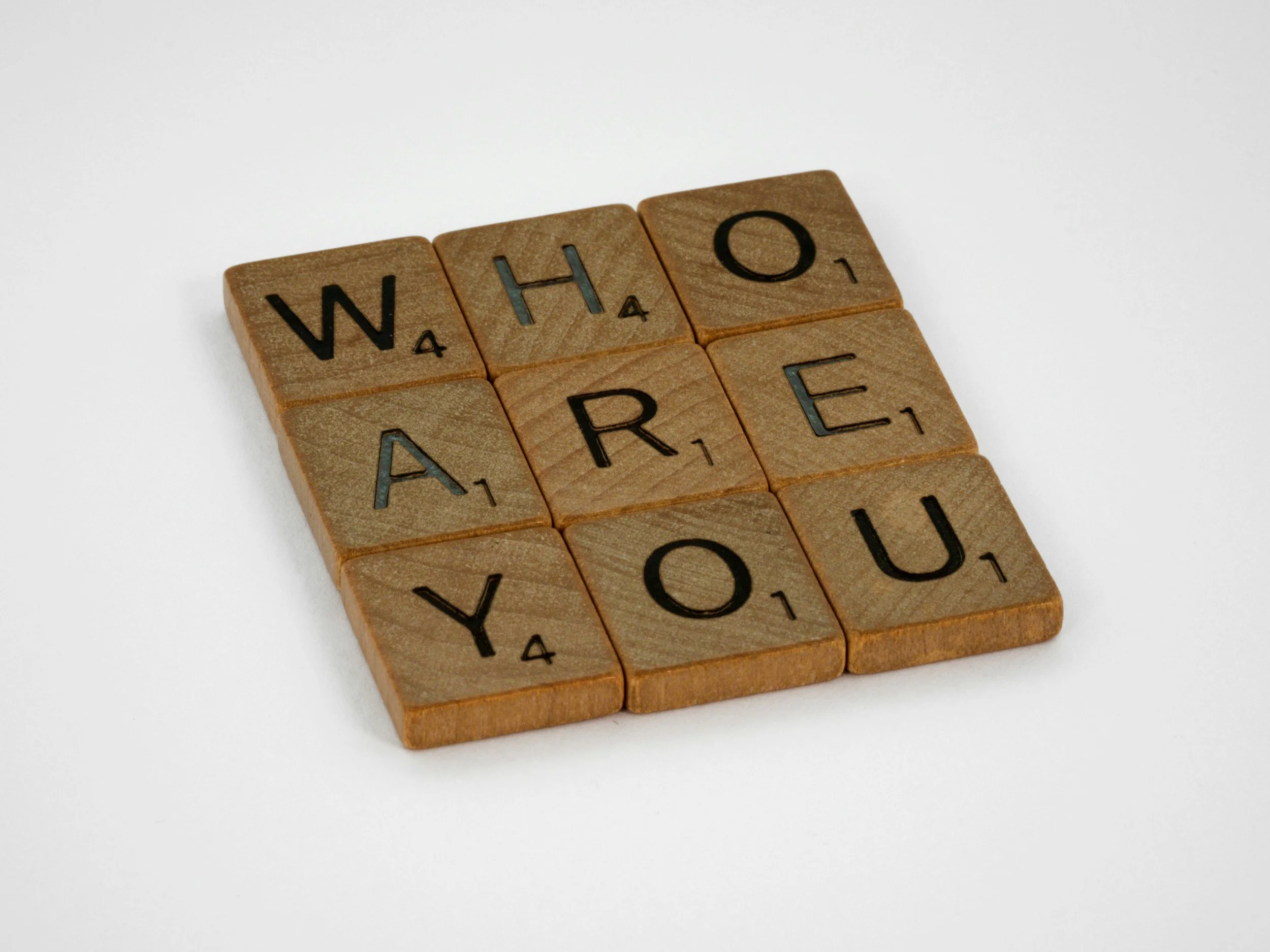 Wooden Scrabble tiles spelling out "Who Are You" on a white background.
