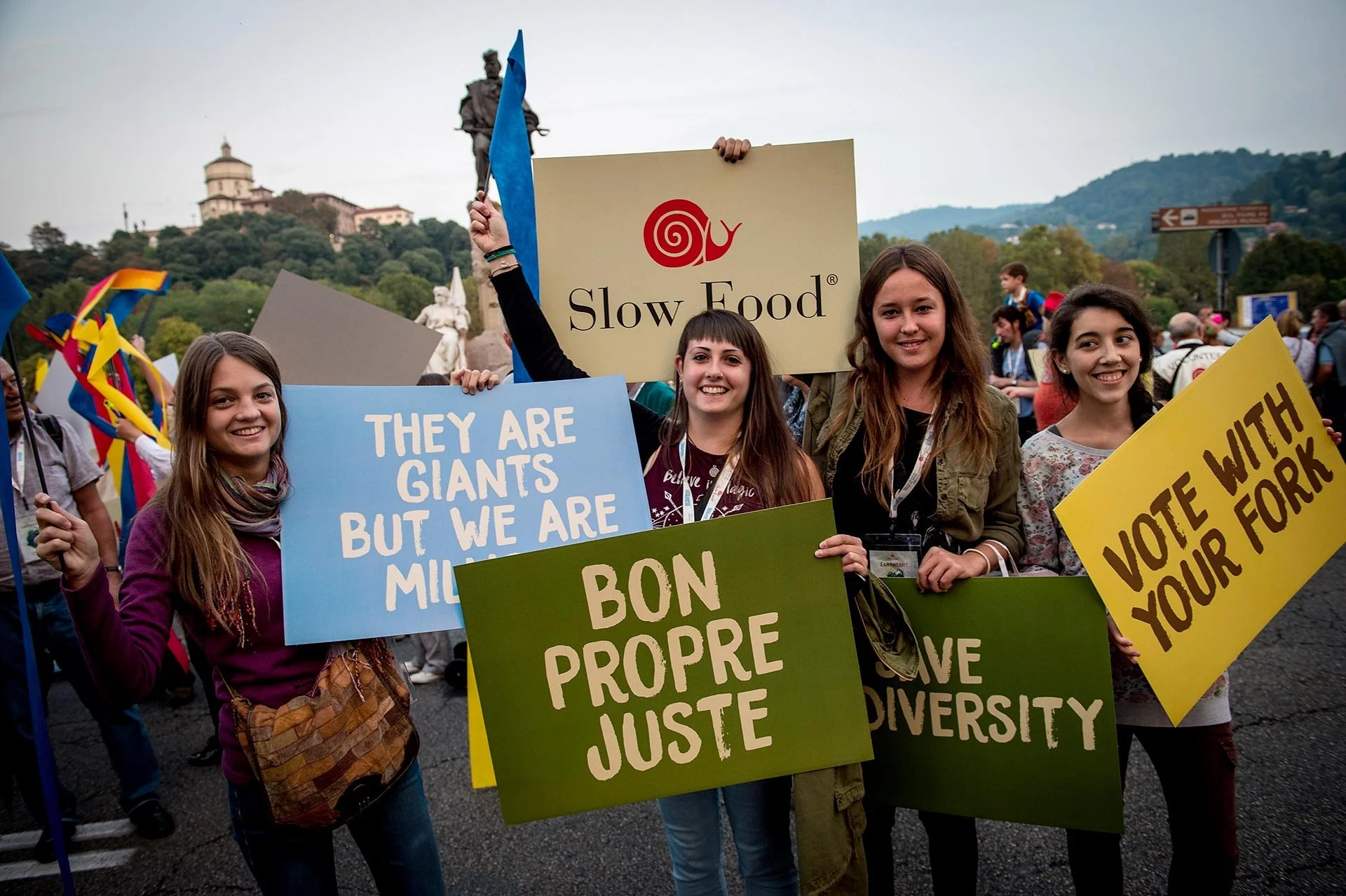 Four young women protesting with signs, one sign reads 'Slow Food,' another 'They are giants but we are mil',