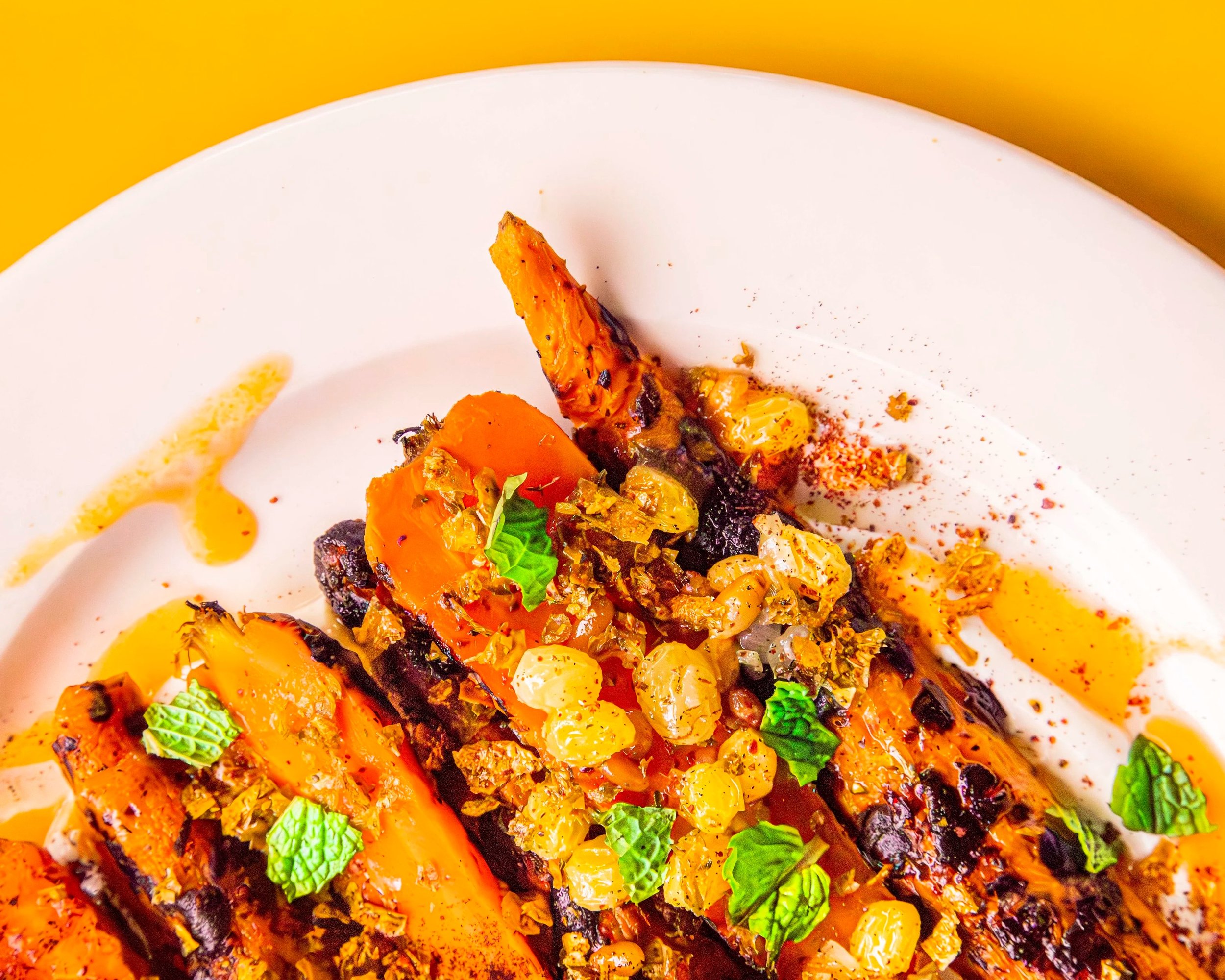 Close-up of a healthy roasted vegetable dish with carrots, garnished with fresh green herbs, drizzled with oil and sprinkled with spices on a white plate.