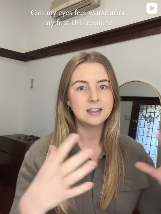A young woman with long blonde hair speaking in a room with white walls, a wooden trim, and a mirror. There is a dresser and a window with decorative glass. Text at the top asks, "Can my eyes feel worse after my first IPL session?".