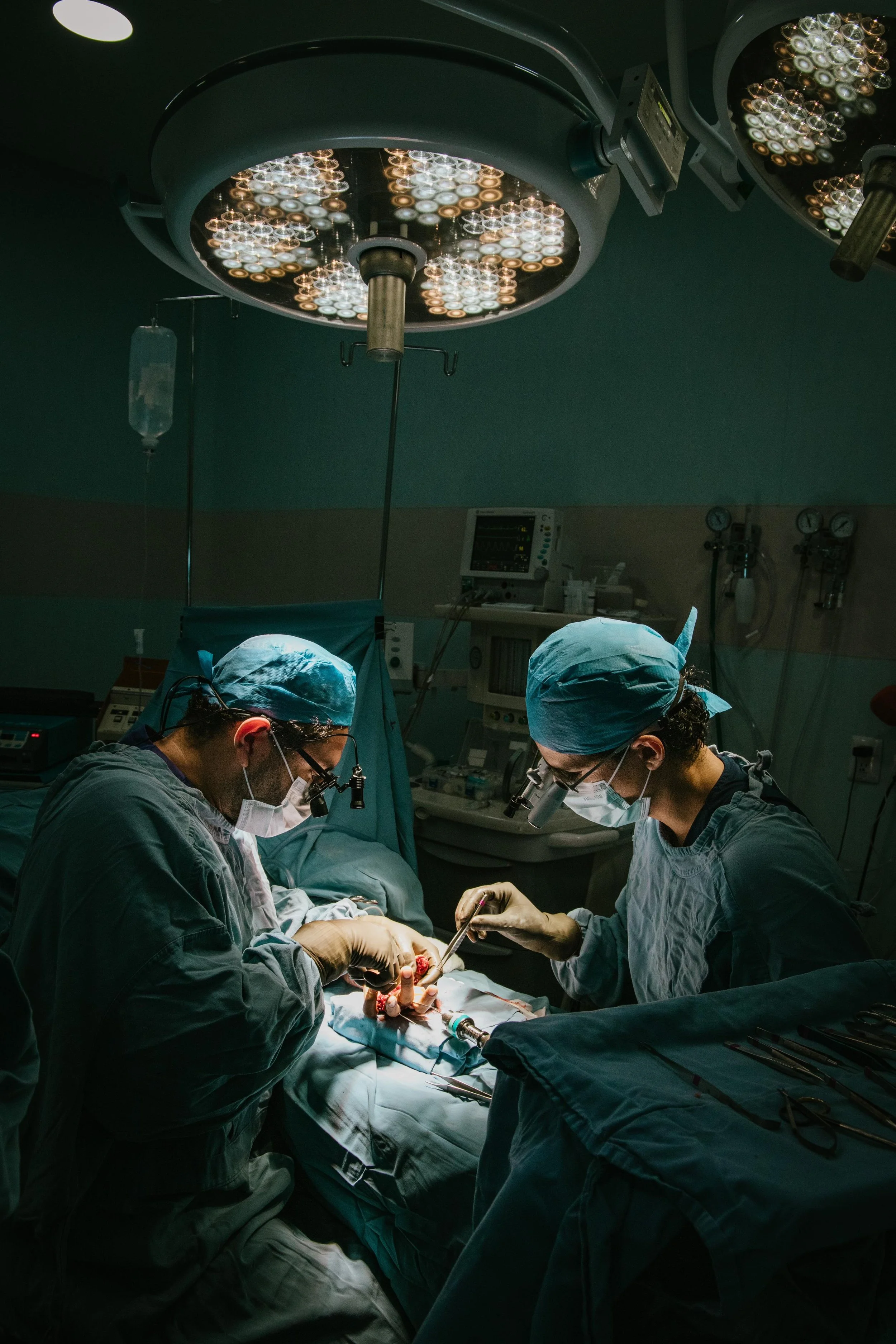 Fotografía en quirófano donde Dos cirujanos  estan realizando una operación en un quirófano con iluminación quirúrgica y equipo médico.