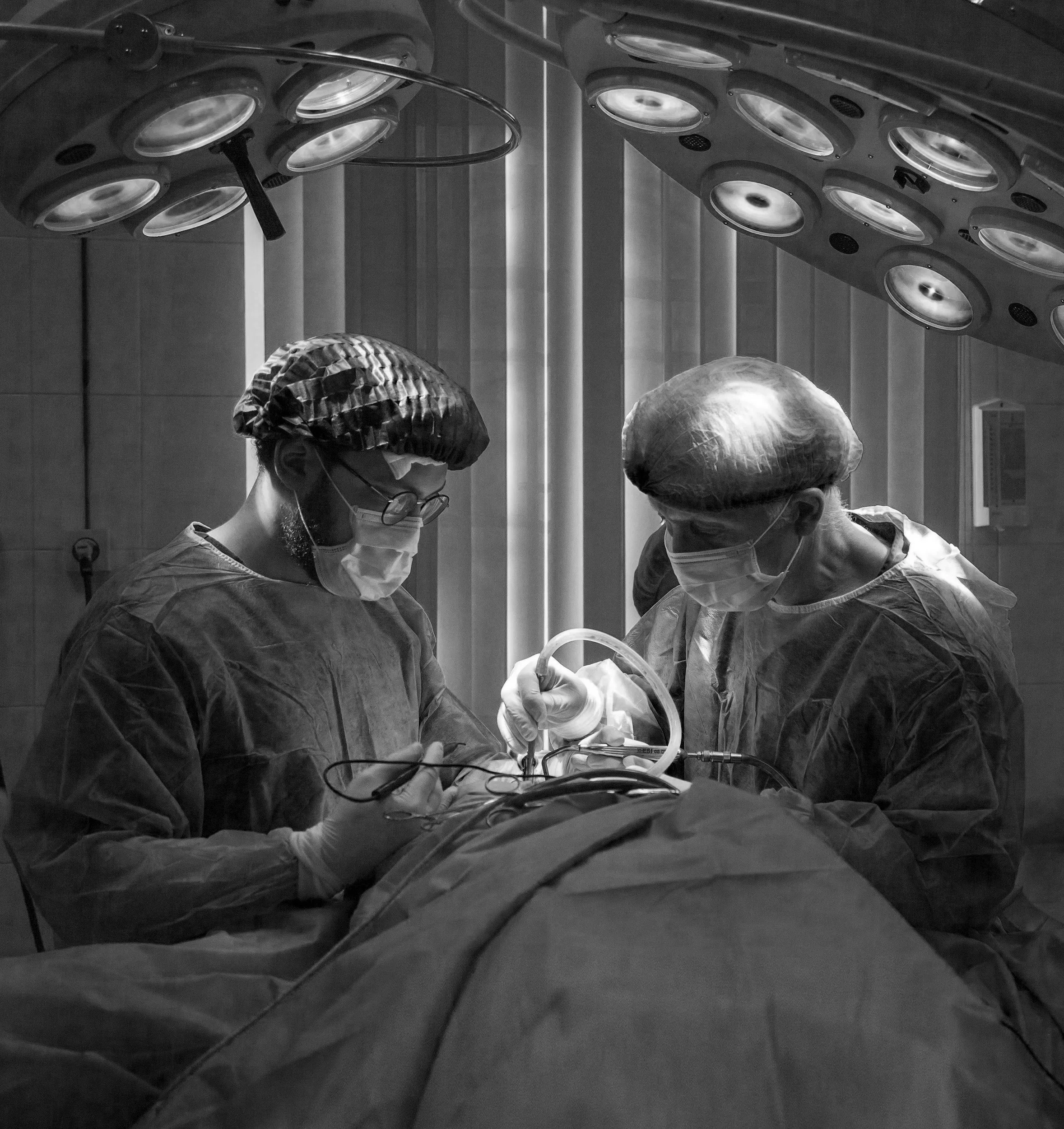 Dos cirujanos en un quirófano realizando una operación con iluminación sobre un paciente.