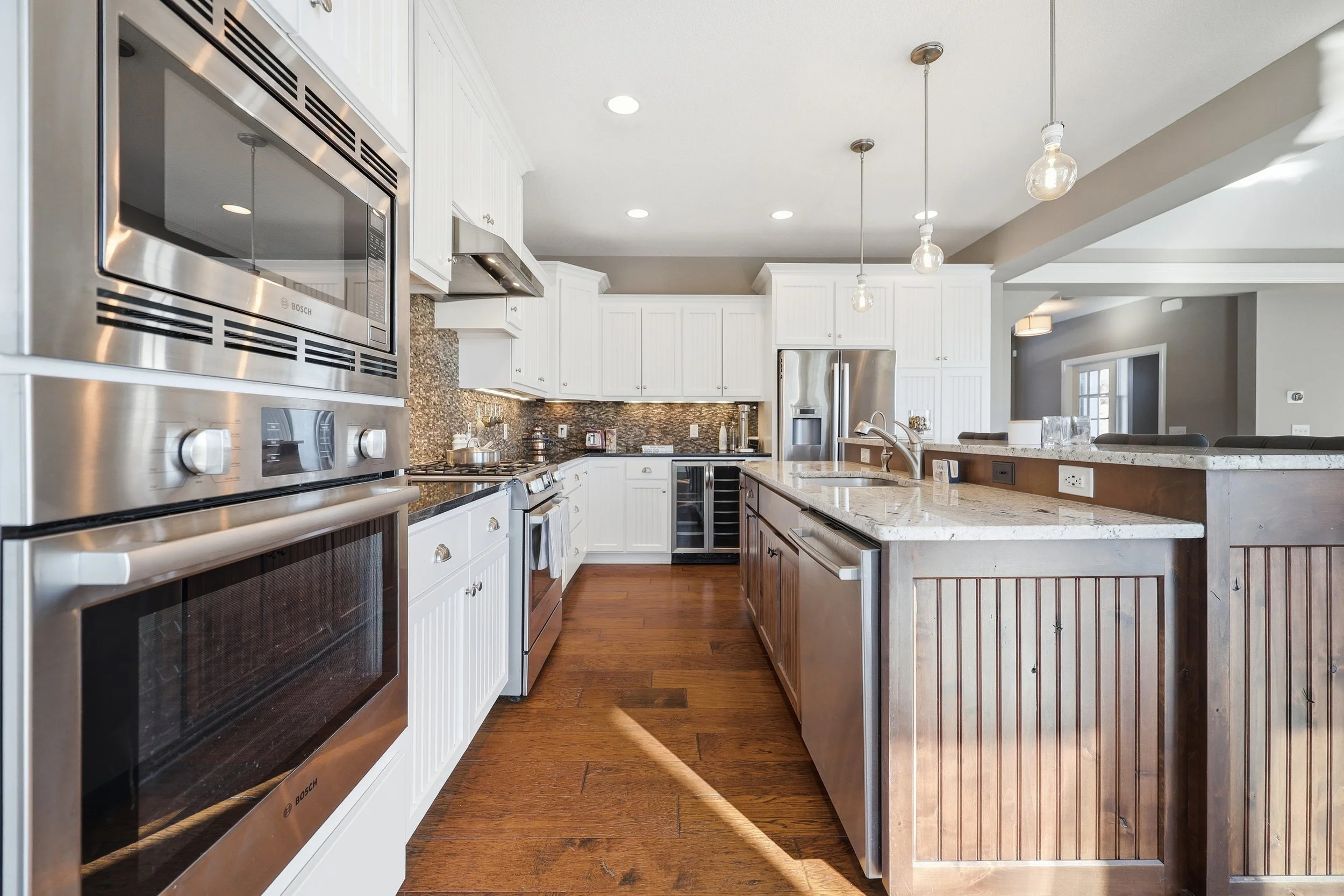 Modern kitchen with white cabinets, stainless steel appliances, granite countertops, and hardwood floors.