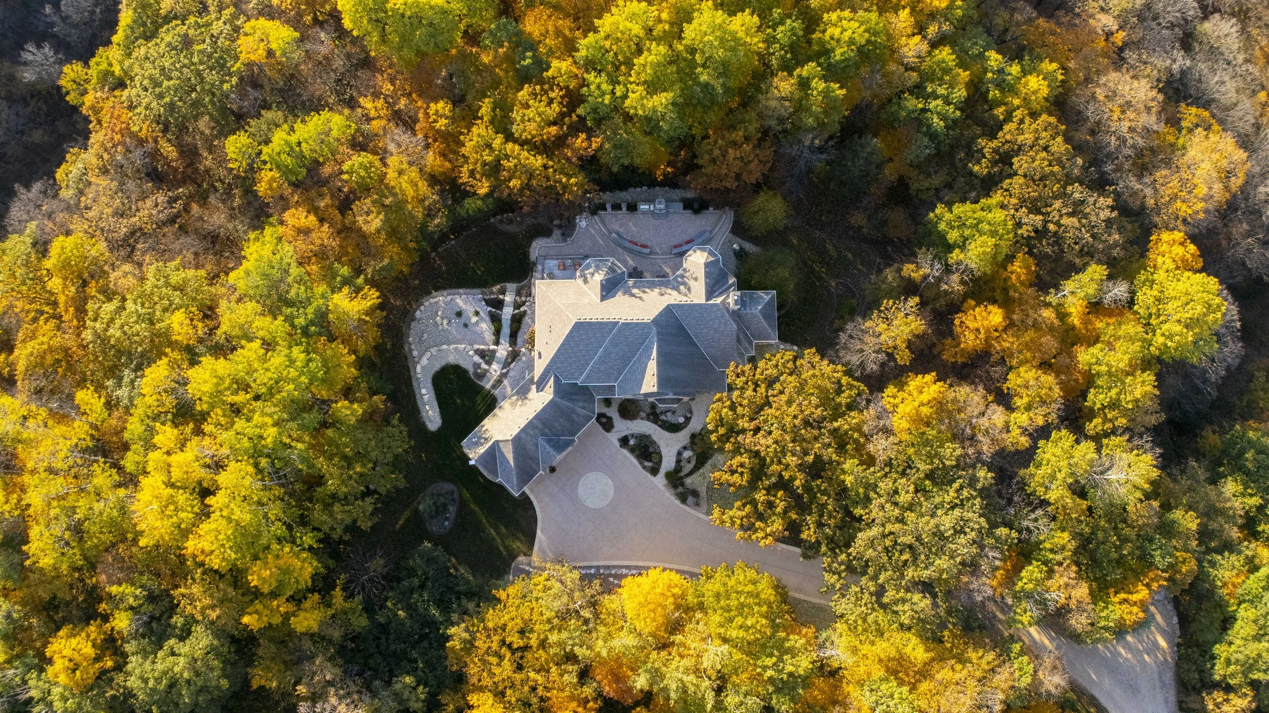 An aerial view of a house surrounded by fall-colored trees with yellow, orange, and green leaves.