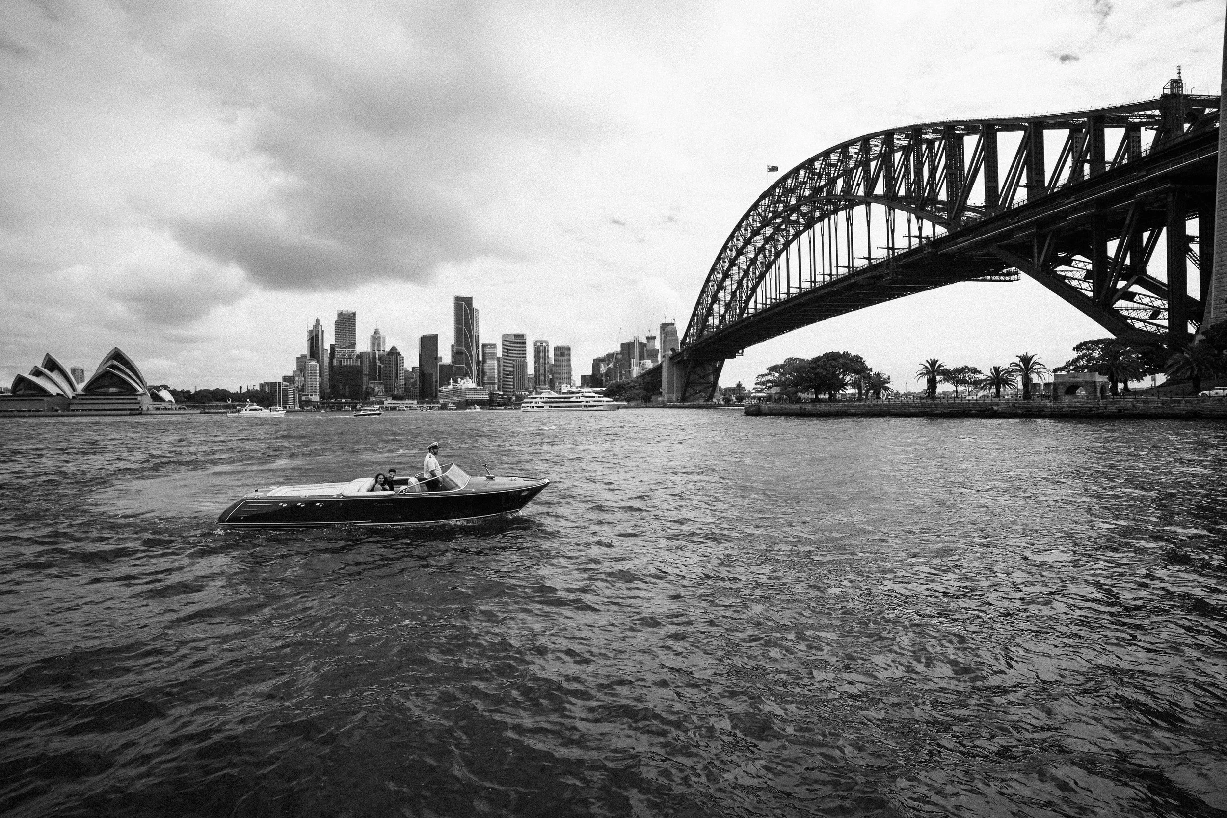 A boat on the water in front of the Sydney skyline and Harbour Bridge in black and white.