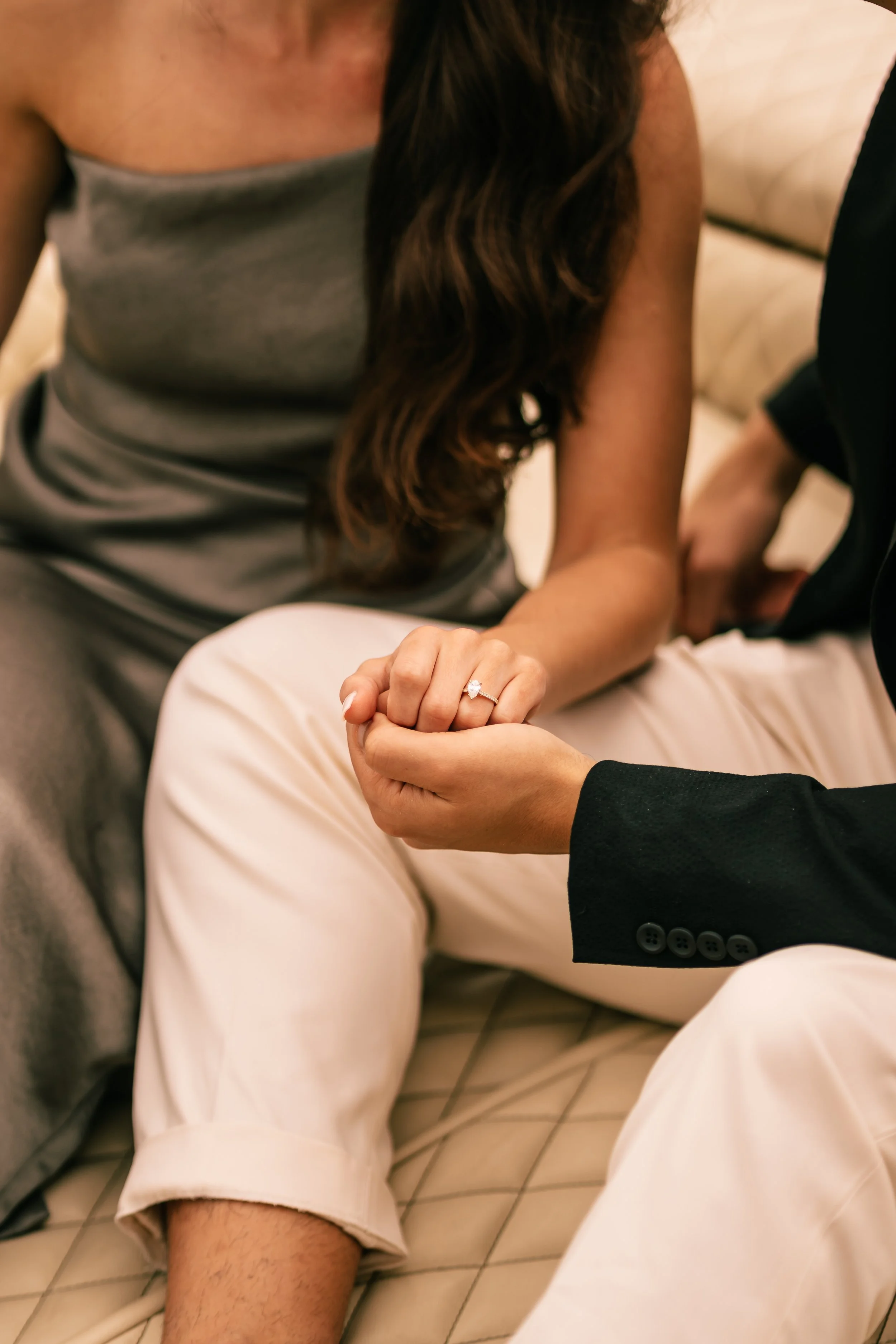 A woman displaying a wedding ring on her finger while sitting with a man, who is holding her hand, in an intimate setting.