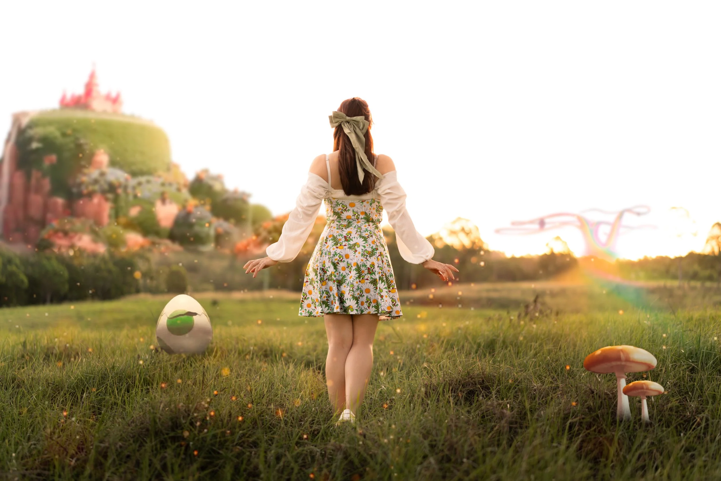 A woman in a floral dress and white shirt with open shoulders, standing on grass in a fantasy landscape with mushrooms, glowing particles, and a colorful dragon-like creature flying in the sky at sunset.