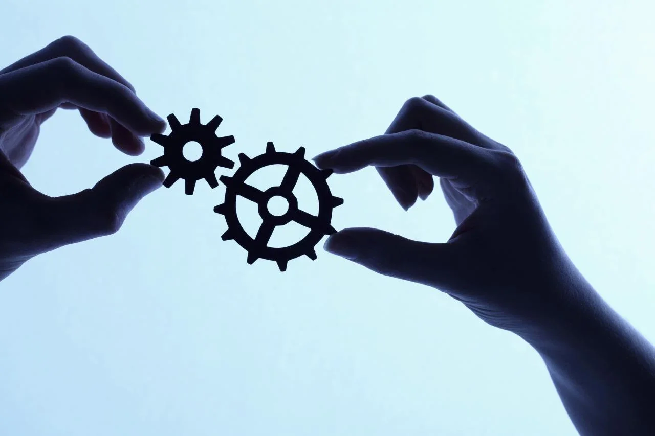 Deux mains manipulent des engrenages en forme de cœurs contre un fond lumineux, symbolisant la connexion ou la collaboration.