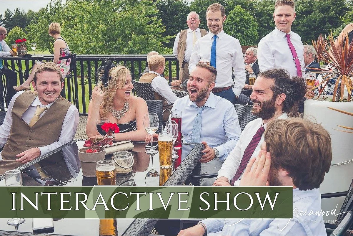 A group of people in formal attire enjoying a gathering outdoors, sitting around a table with drinks, some laughing and smiling, with trees in the background, and the words "INTERACTIVE SHOW" overlaid.