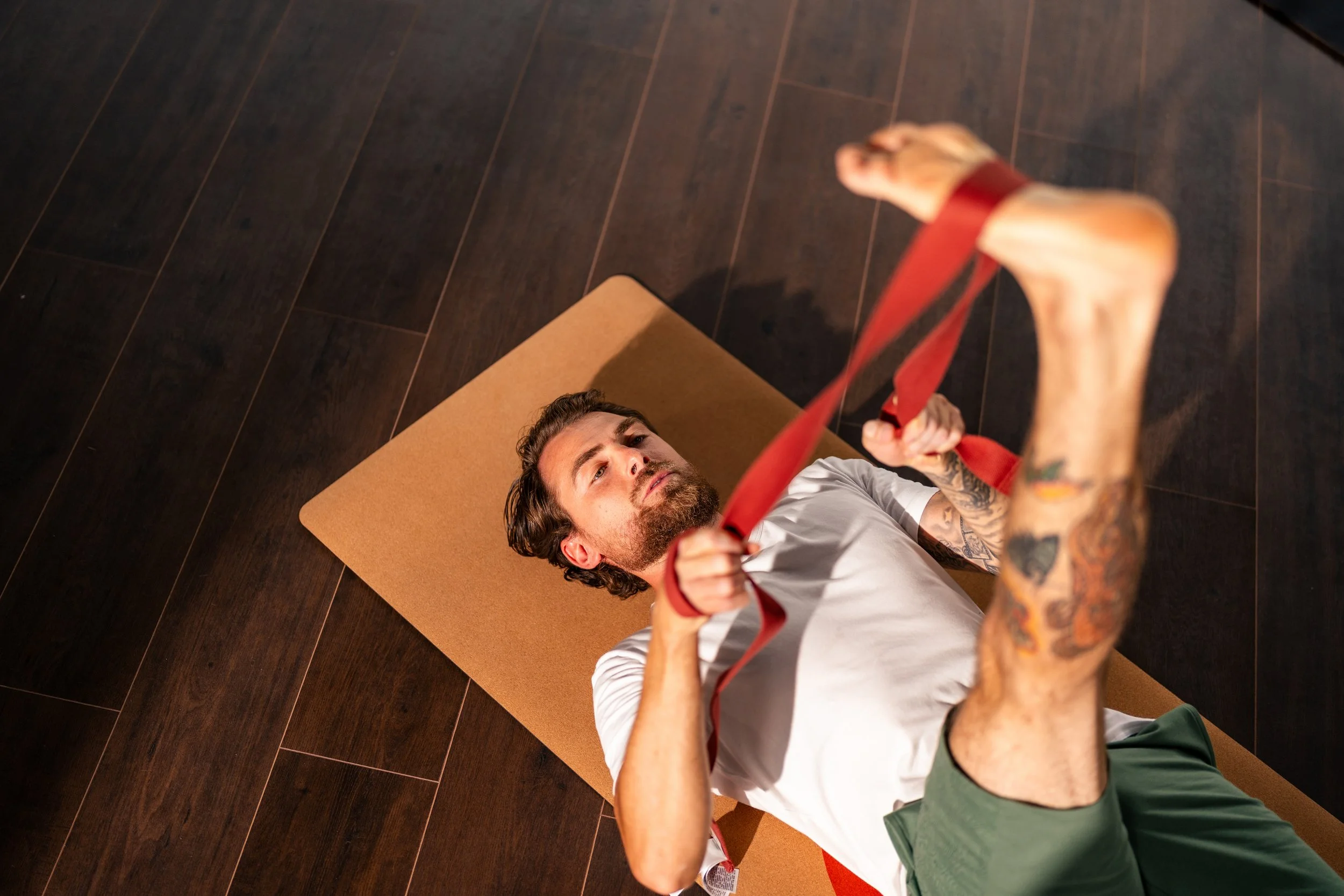 A woman with gray hair is lying on a Pilates reformer machine, performing an exercise. Another woman, likely a trainer, is assisting her.