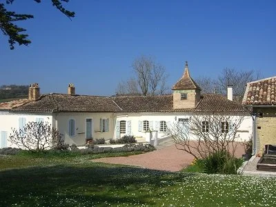 A white building with a tiled roof, small turret, and garden with trees and a pathway under a clear blue sky.