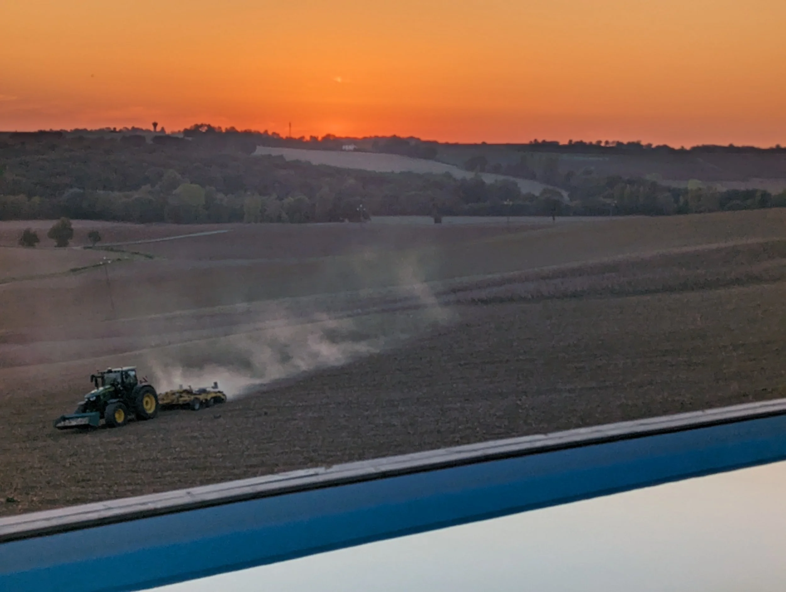 A tractor plowing or planting a field at sunset with a colorful sky in the background.
