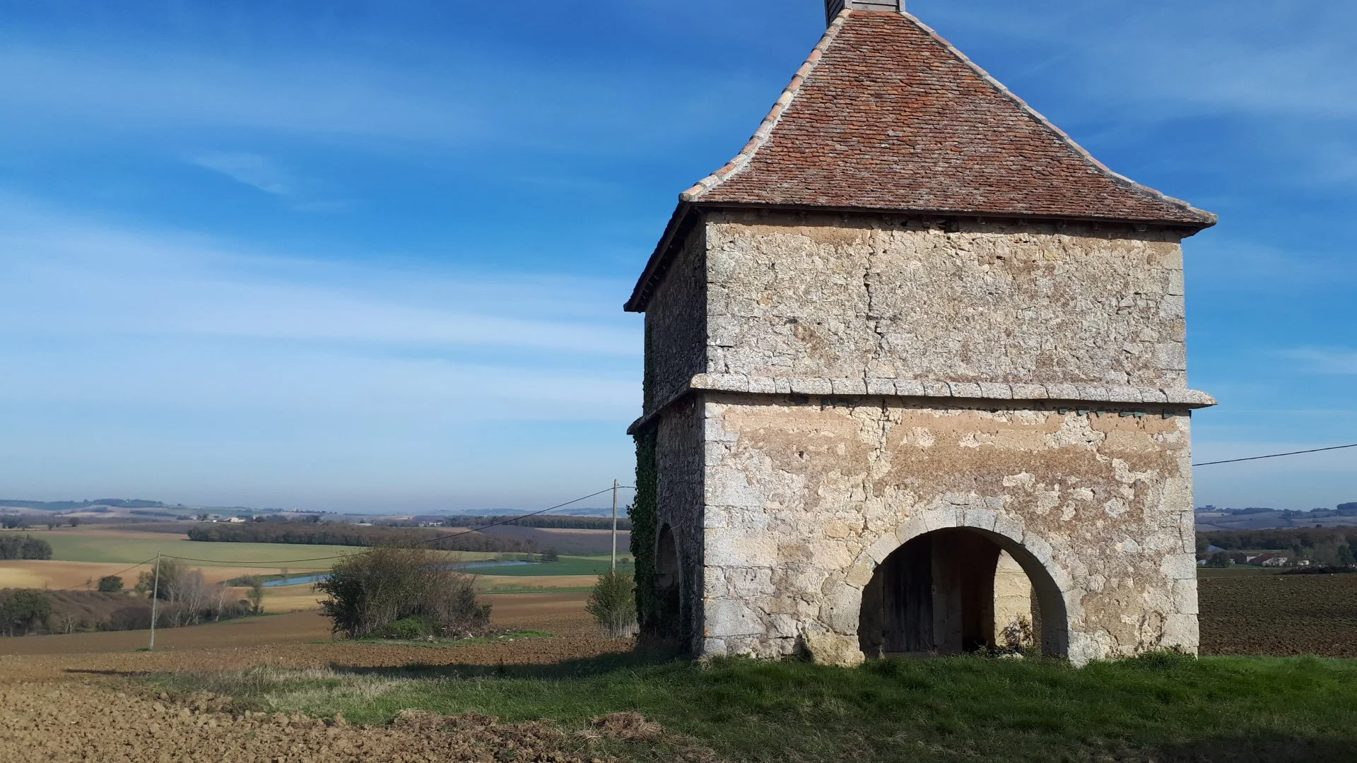 A typical countryside scene in the Gers featuring an old stone pigeonniere which is a classic Gersoise building with a red tile roof.