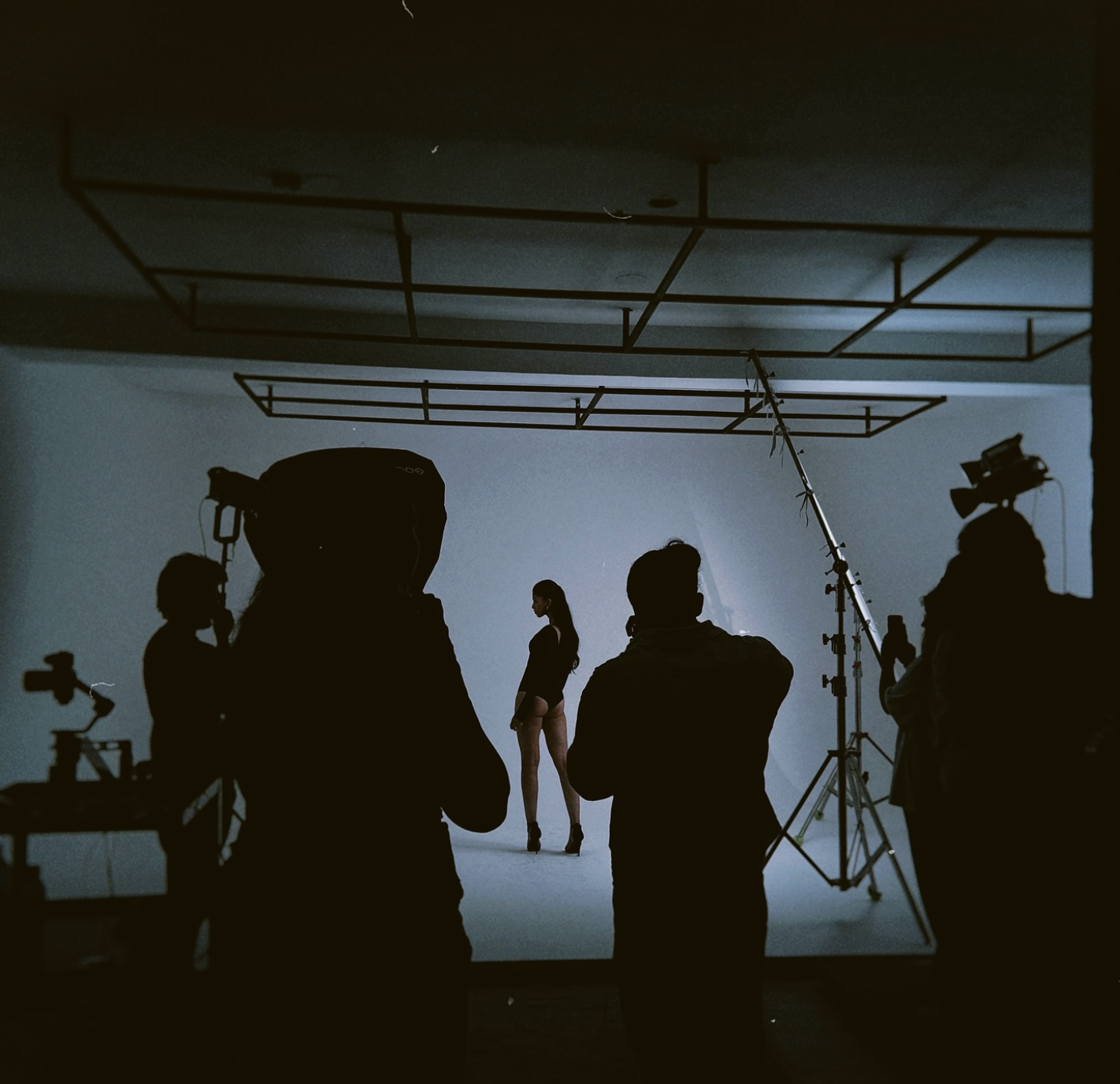Silhouettes of a film crew filming a woman in a photo studio with lighting and equipment.
