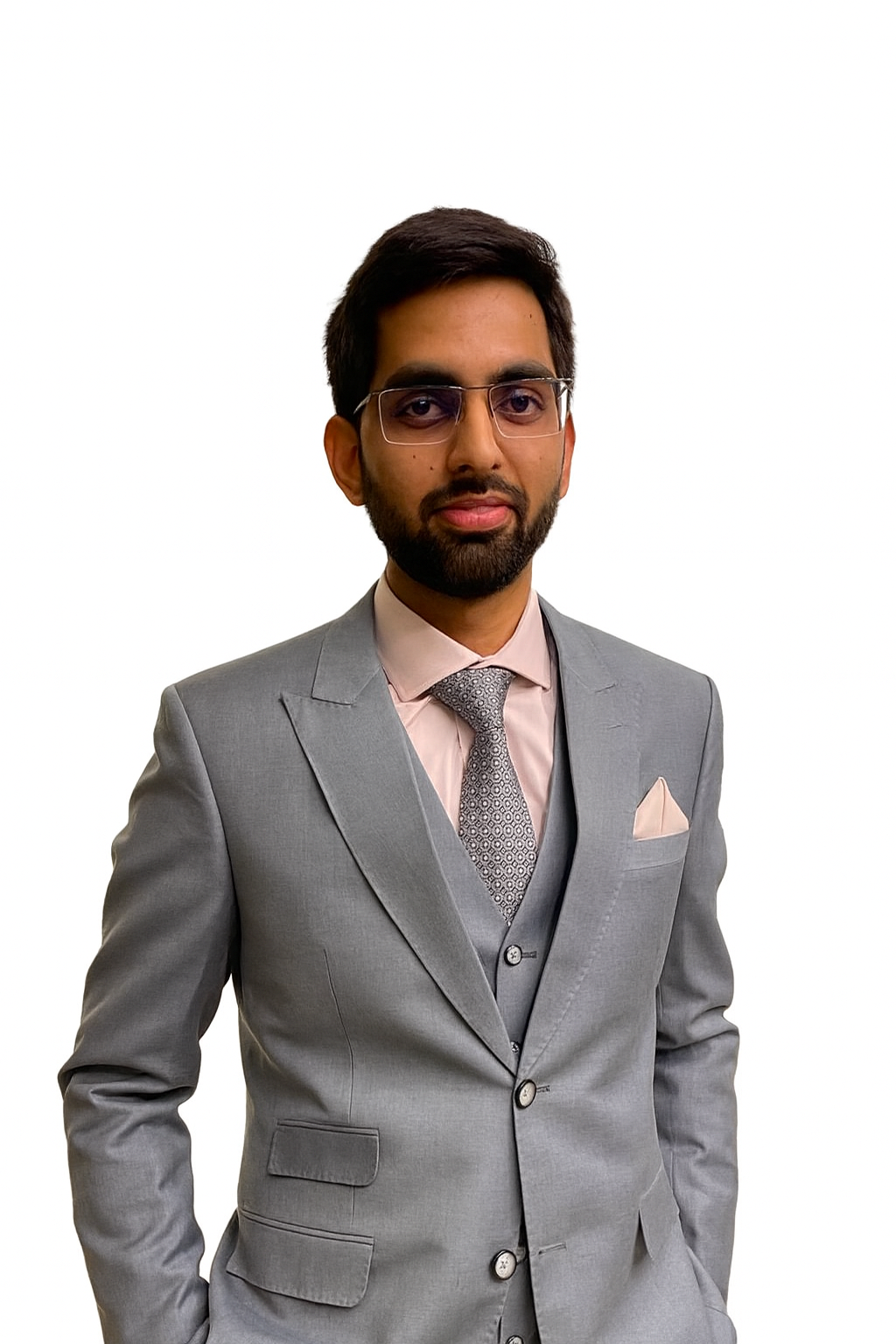 A man wearing a grey suit with a pink dress shirt and patterned tie, standing against a plain white background.