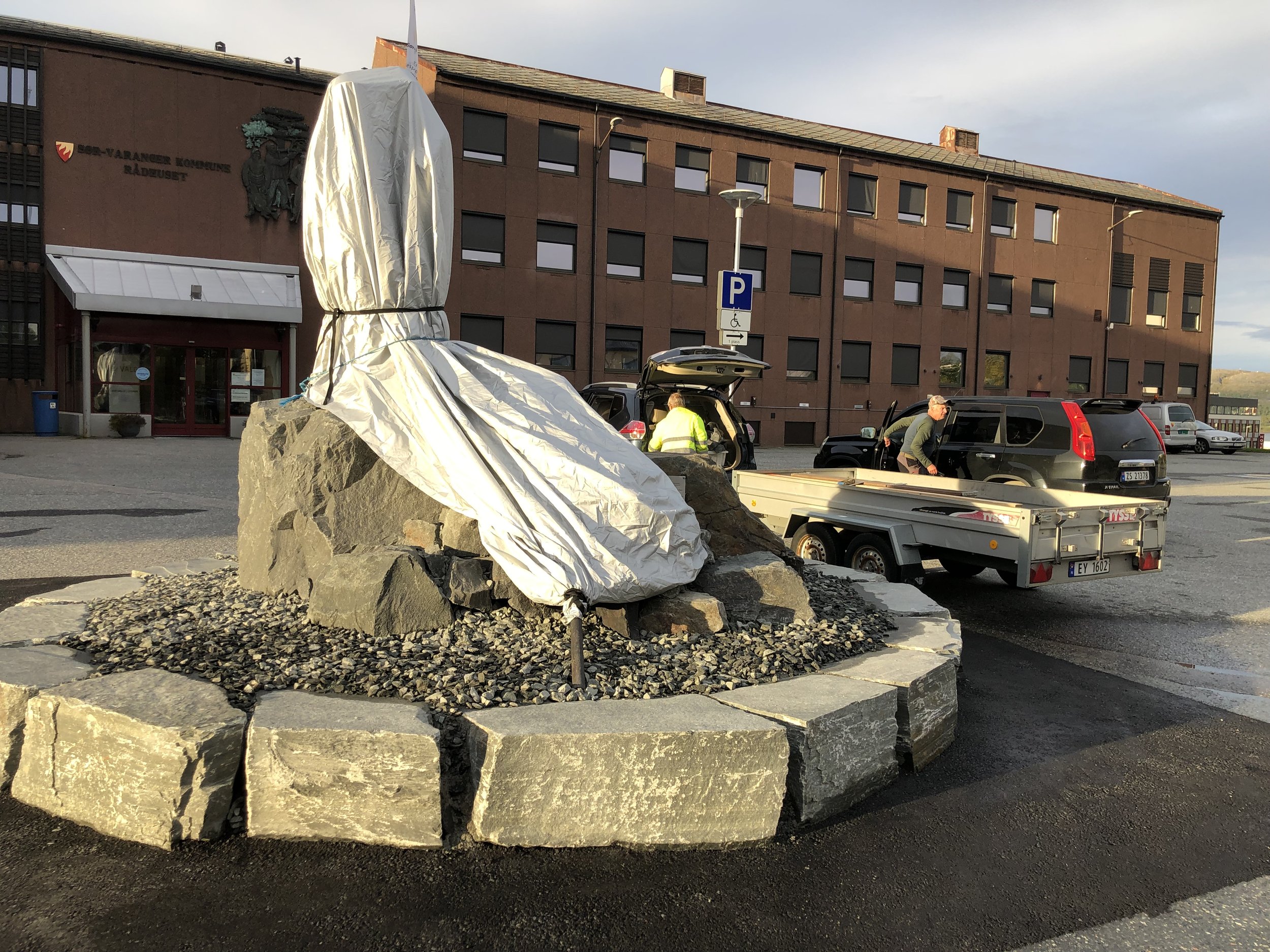 Minnesmerket - med fane og figurer - er klargjort og tildekket dagen før avdukingen 8. september 2023. Charles Mortensen og Halle Mikkelborg i bakgrunnen. 