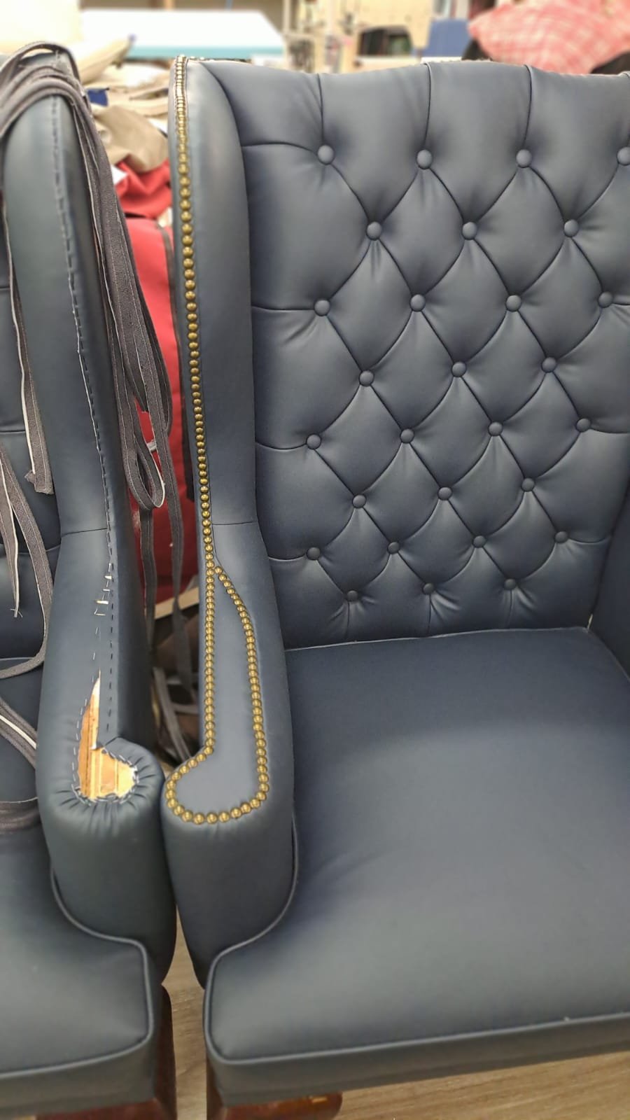A navy blue tufted armchair with gold nailhead trim along the side.