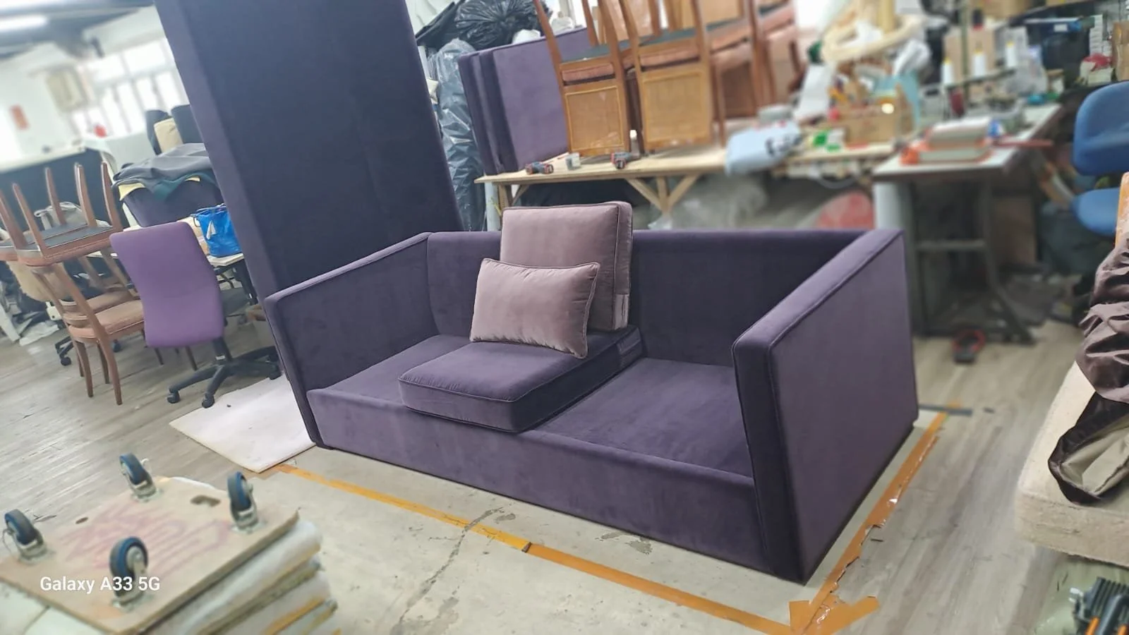 Purple velvet sofa with two cushions in a cluttered furniture workshop or warehouse.