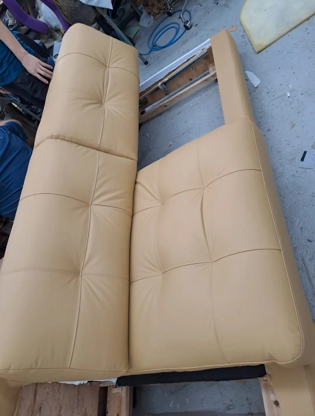 Newly upholstered beige couch with tufted cushions in a workshop setting.