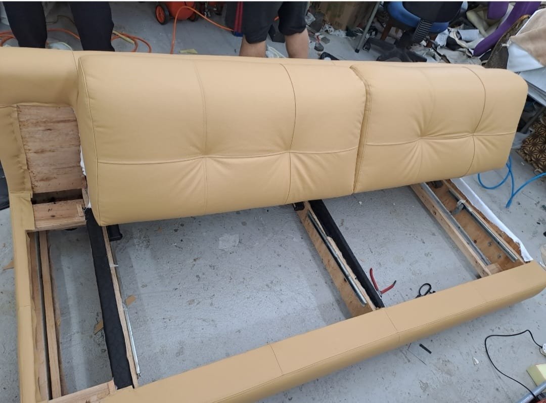 Yellow upholstered sofa in the process of being repaired or reupholstered, with parts of the frame exposed and some tools nearby.