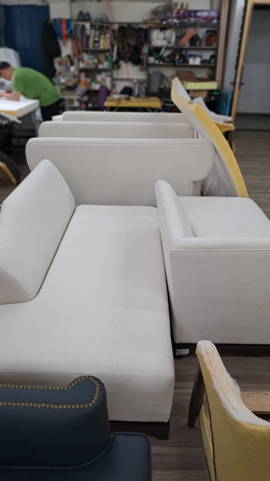 White upholstered sectional sofa in a furniture store with various chairs and cluttered shelves in the background.