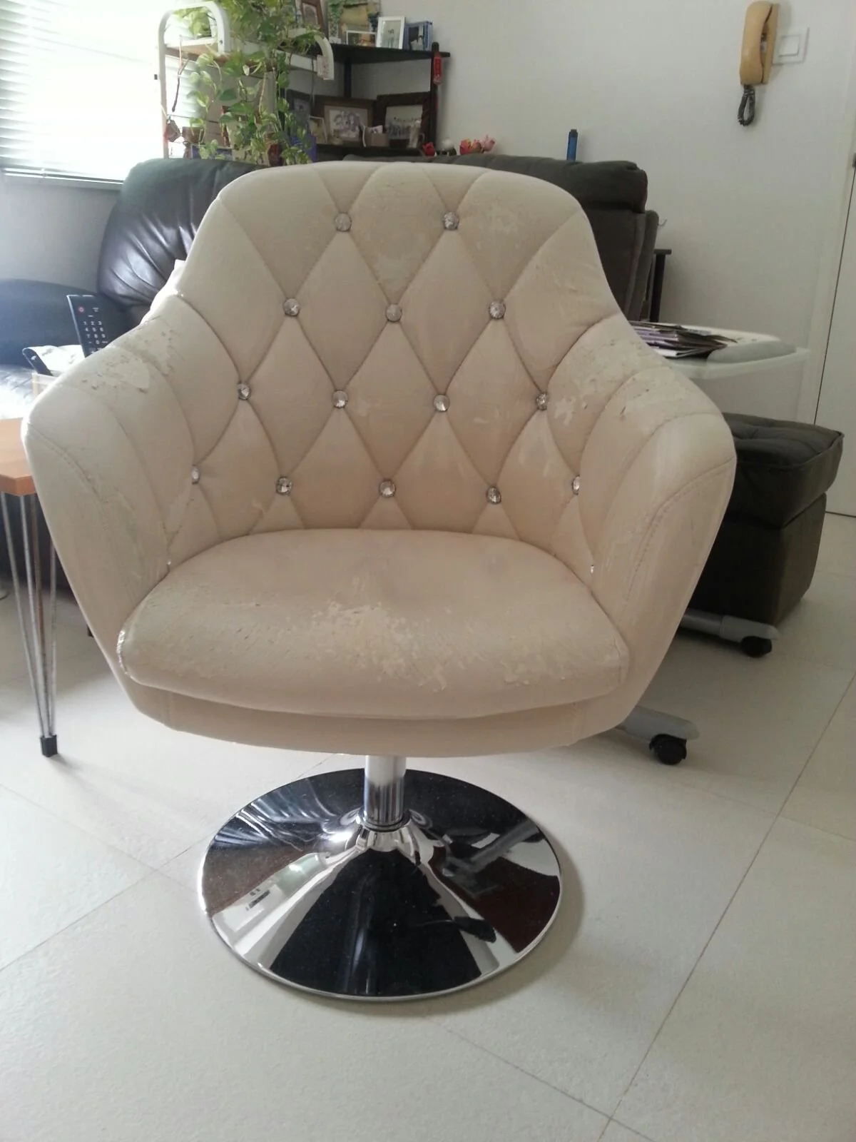 A cream-colored tufted swivel chair with crystal button accents in a living room.