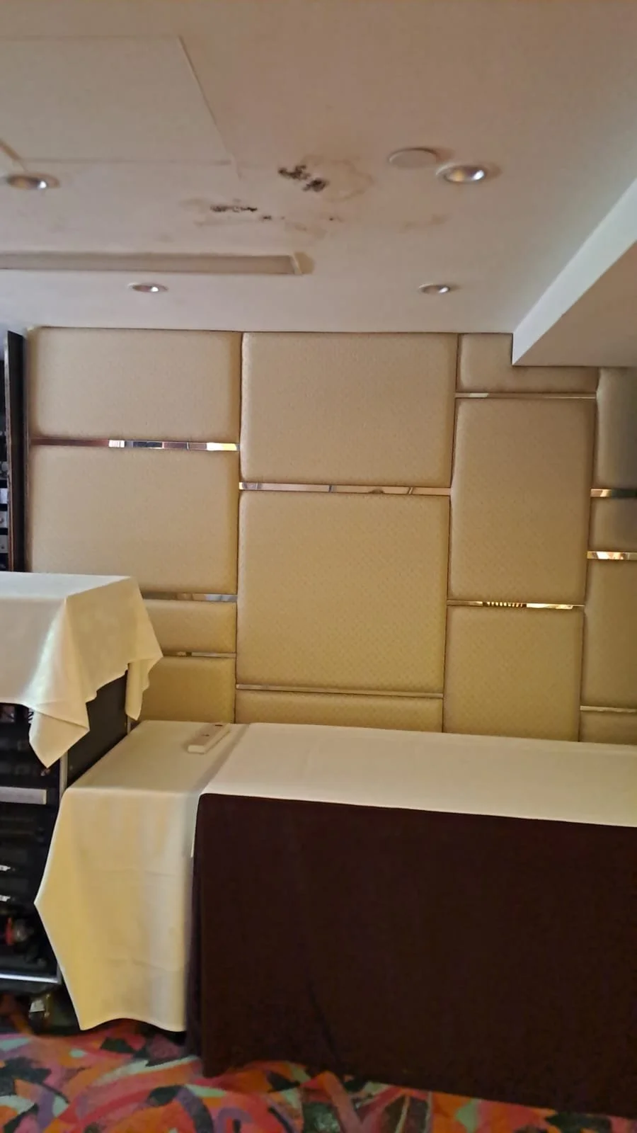 Interior of a restaurant with beige padded wall panels, a table with a white tablecloth, and a colorful carpet.