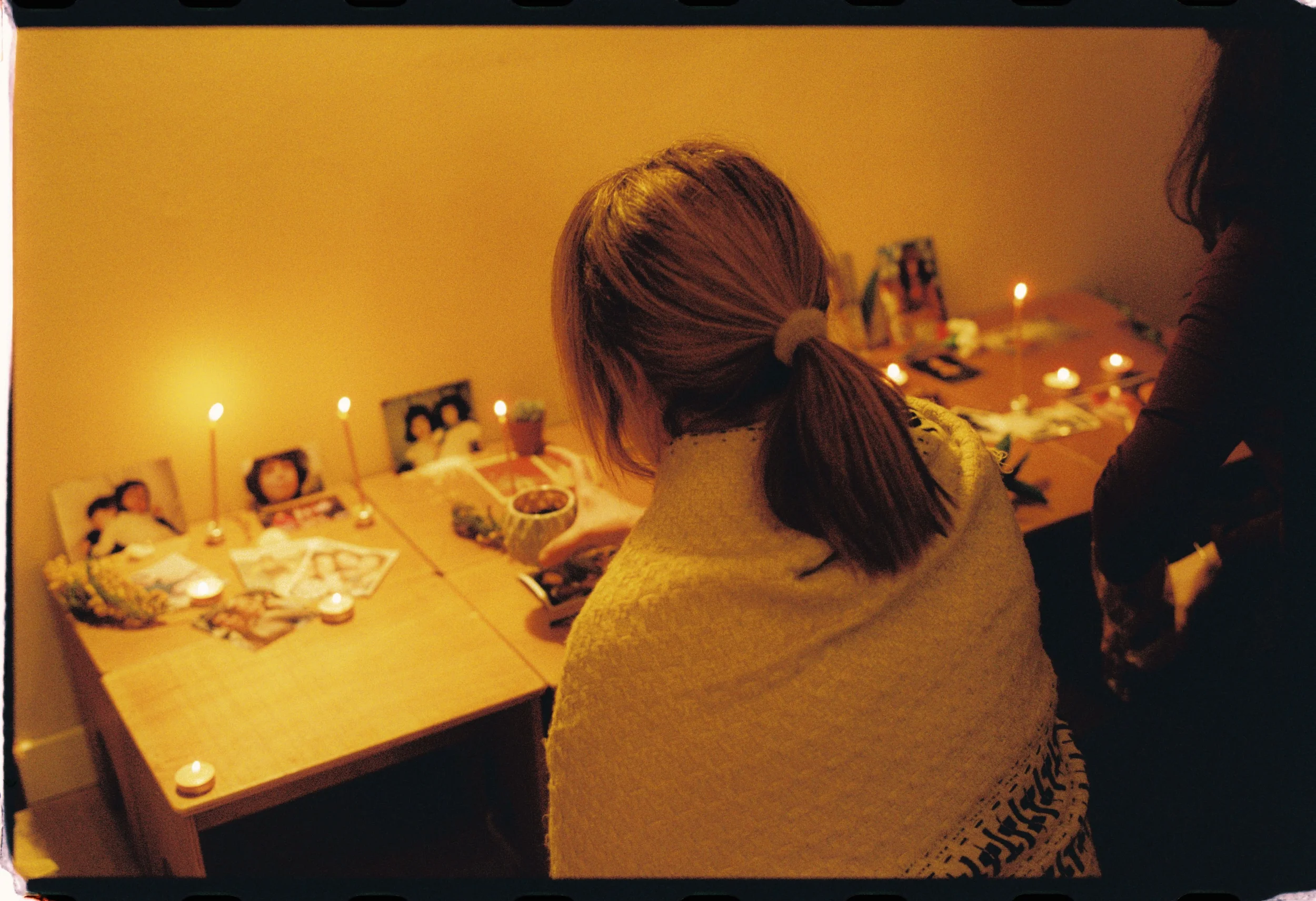 Cena de varias personas participando en una ceremonia en un ambiente íntimo, con velas encendidas y fotografías en la pared, en un entorno acogedor y decorado con flores y objetos religiosos.