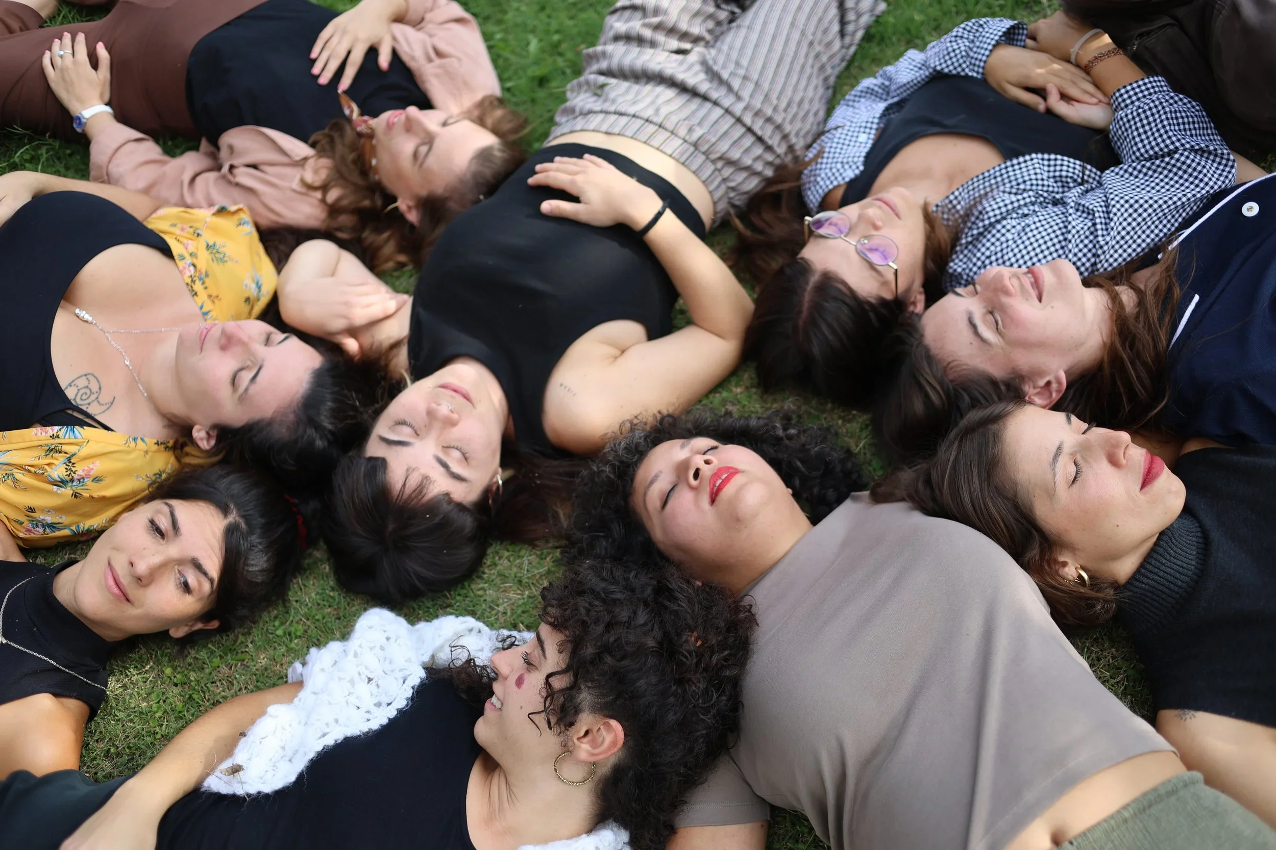 Grupo de personas acostadas en el césped con los ojos cerrados, parecen relajadas y disfrutando del momento.