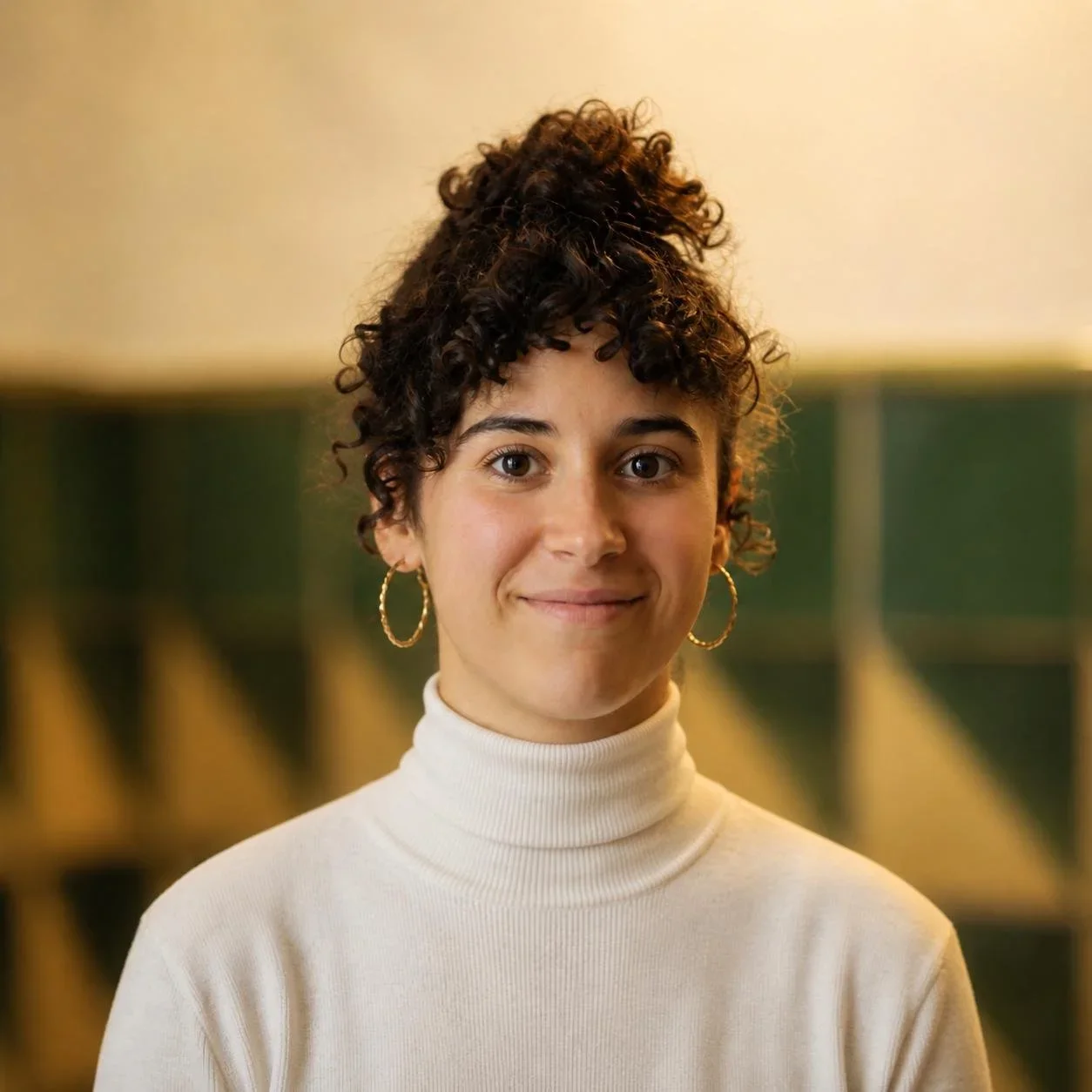 Retrato de una mujer joven con cabello rizado y oscuro, usando un suéter de cuello alto blanco y aretes de aro dorados, en un fondo difuso con estanterías verdes.