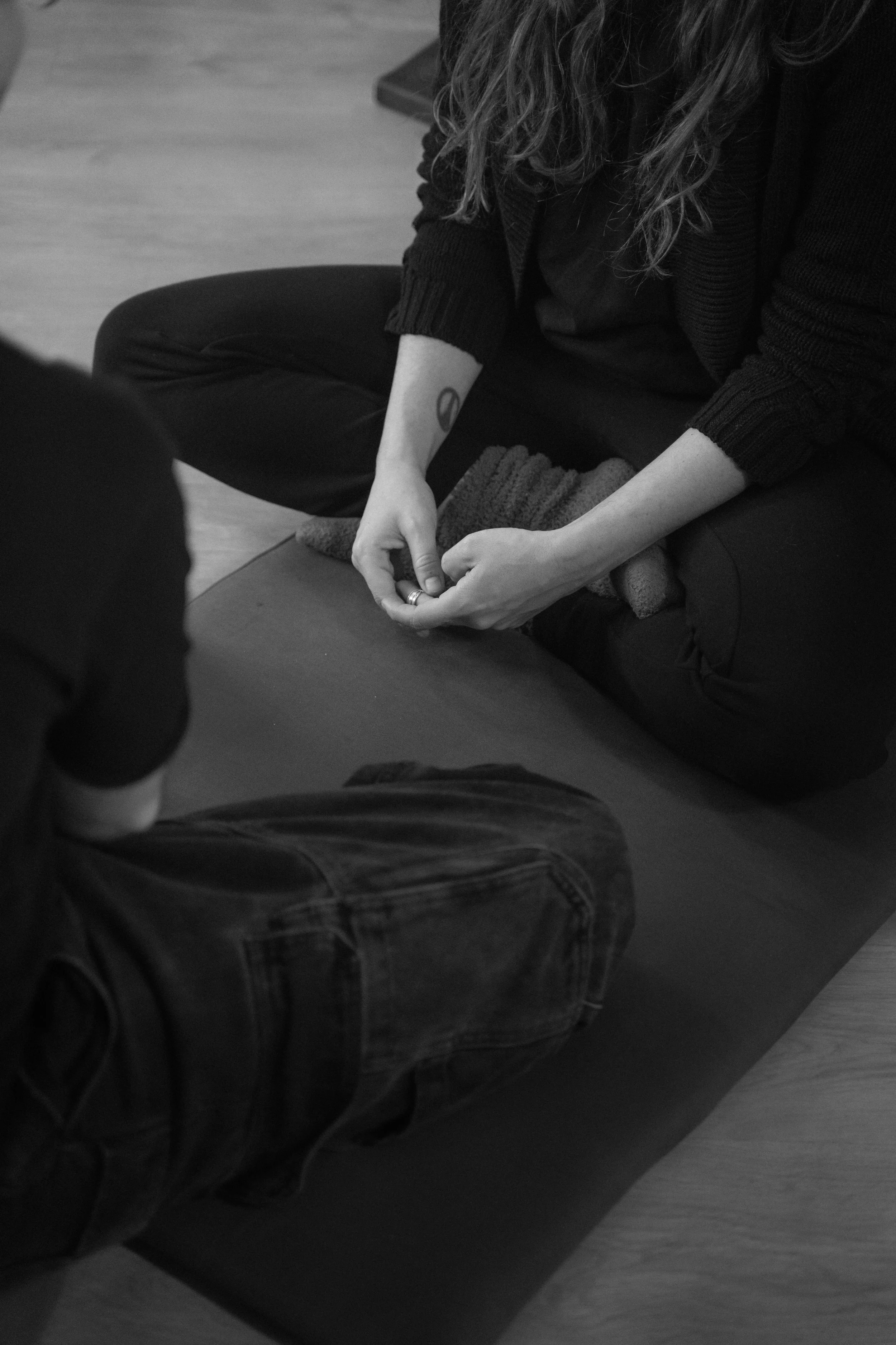 Persona con cabello rizado, vestida de negro, en posición de yoga en un tapete en interiores.