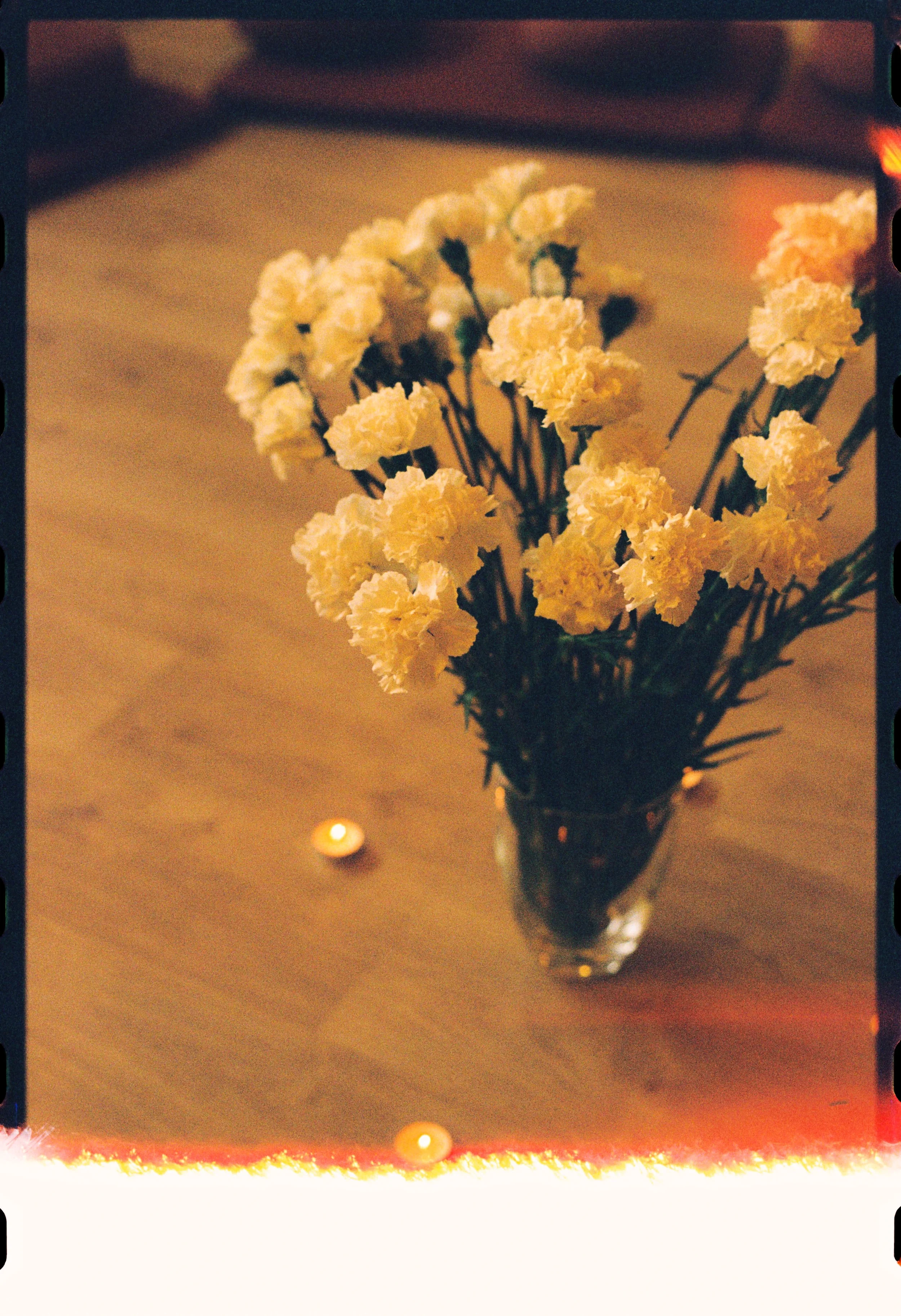 Ramo de flores blancas en un jarrón de vidrio en una mesa de madera con una vela encendida cerca.