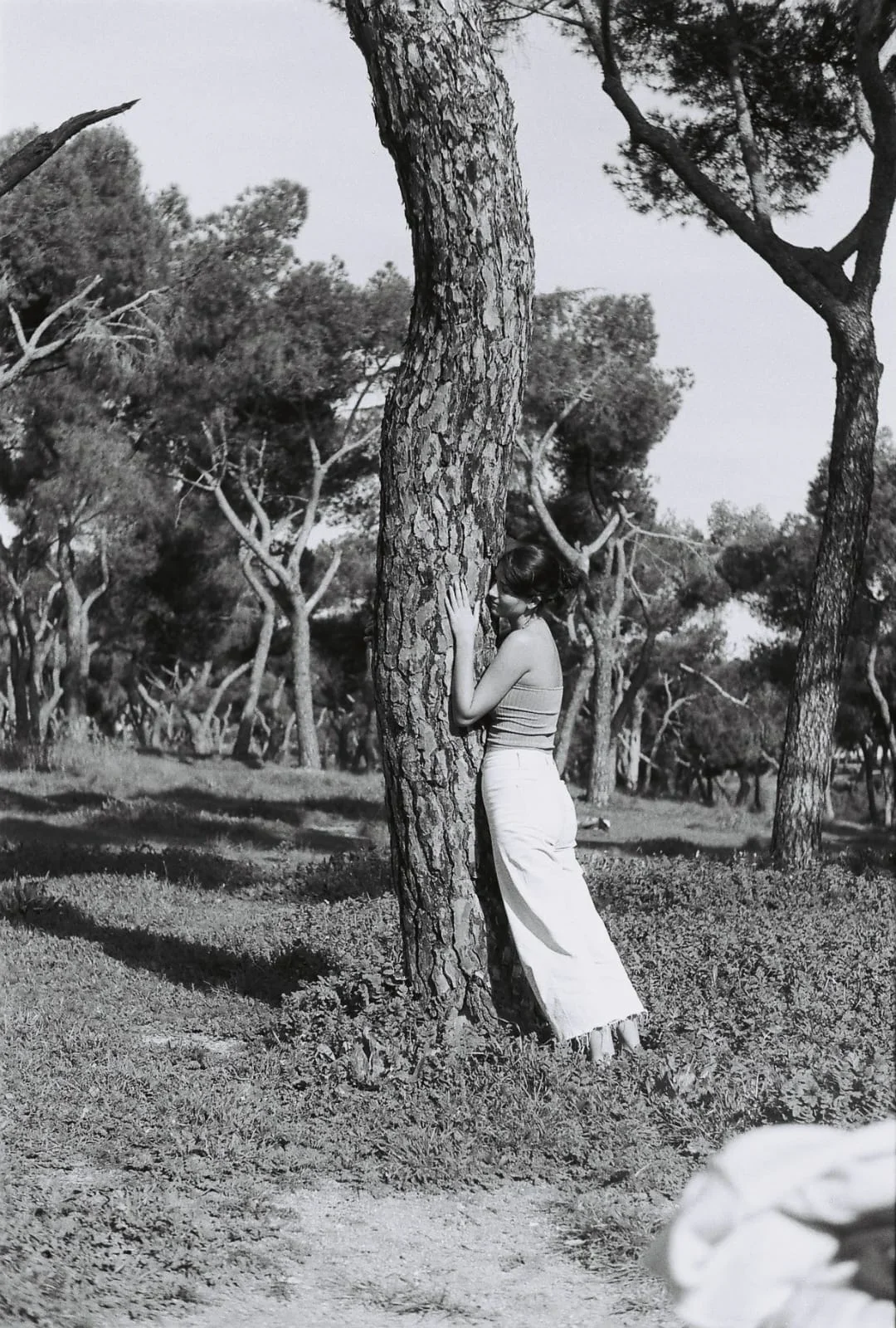 Una mujer en un bosque, abrazando un árbol, en una fotografía en blanco y negro.