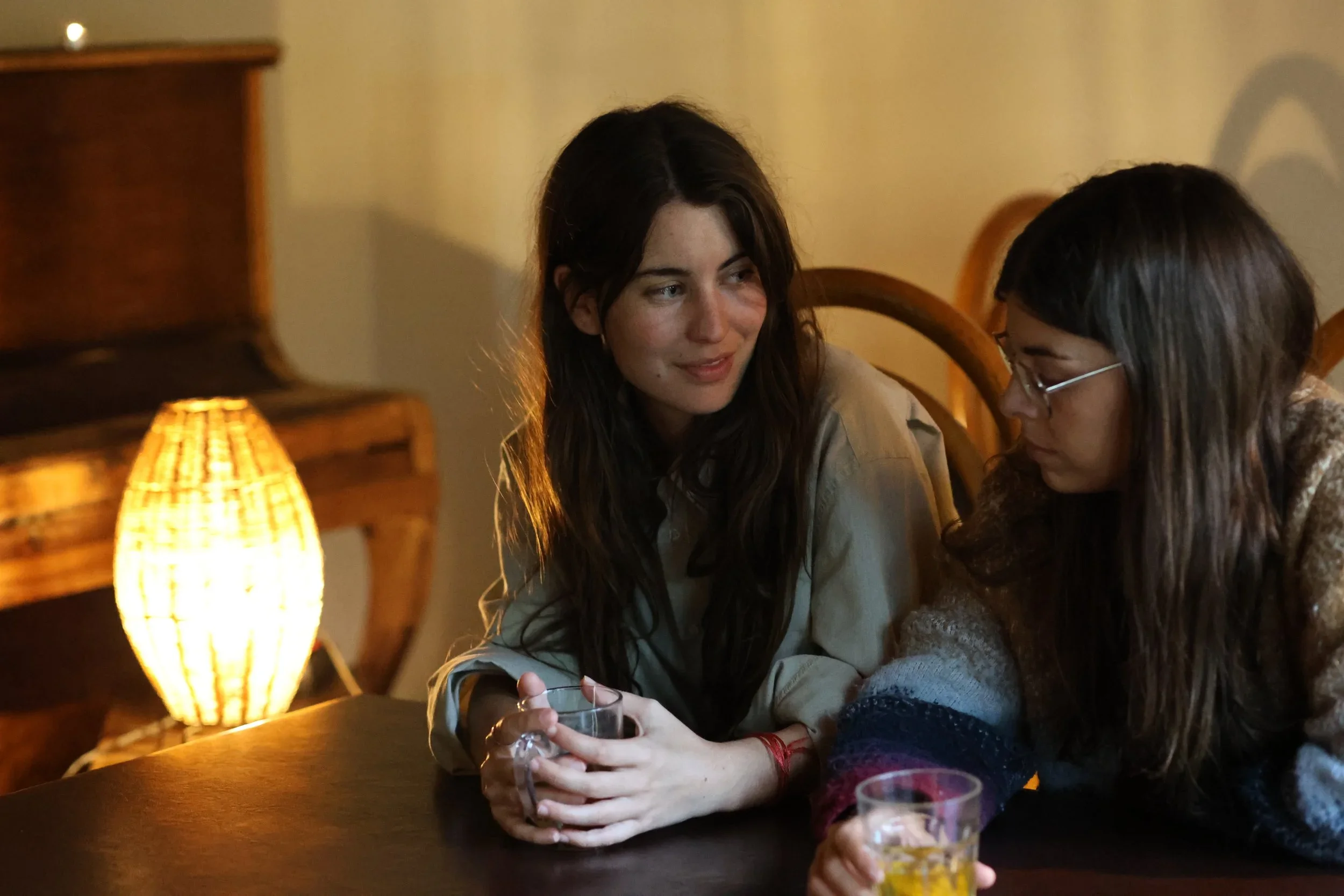 Dos jóvenes conversando en un ambiente cálido y acogedor, iluminado por una lámpara de papel en un entorno íntimo.