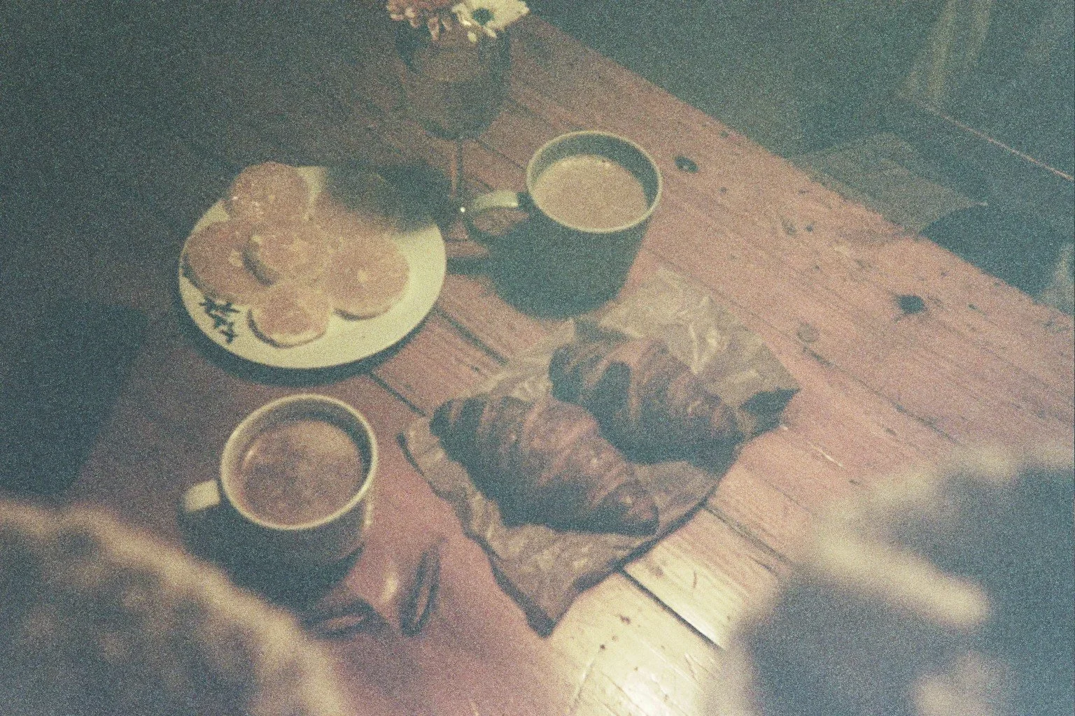 Desayuno con croissants, café en tazas y galletas con mermelada sobre una mesa de madera.