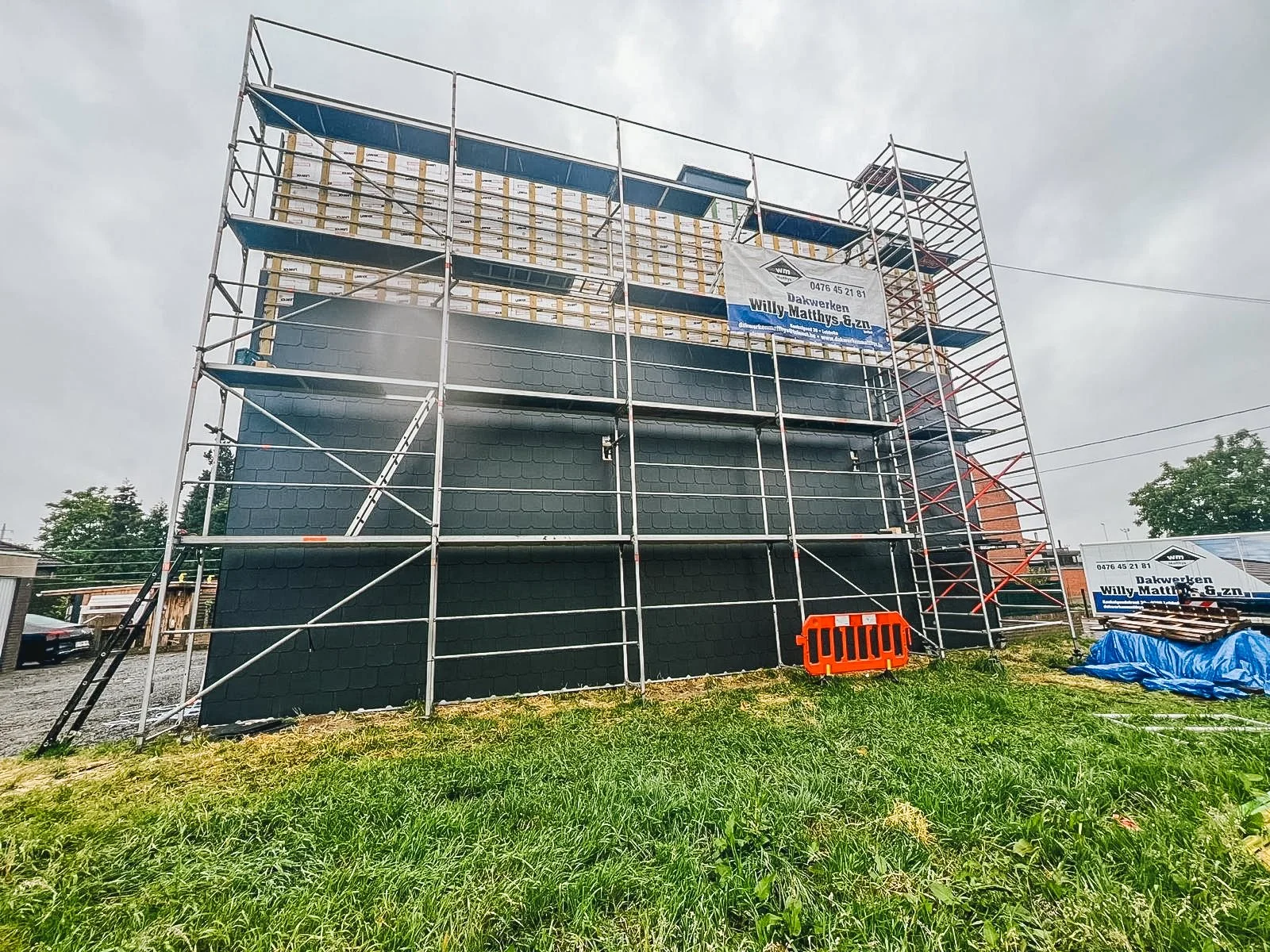 Een bouwsteiger rondom een zwart geschilderd gebouw met een dak dat in aanbouw is, onder een bewolkte hemel.