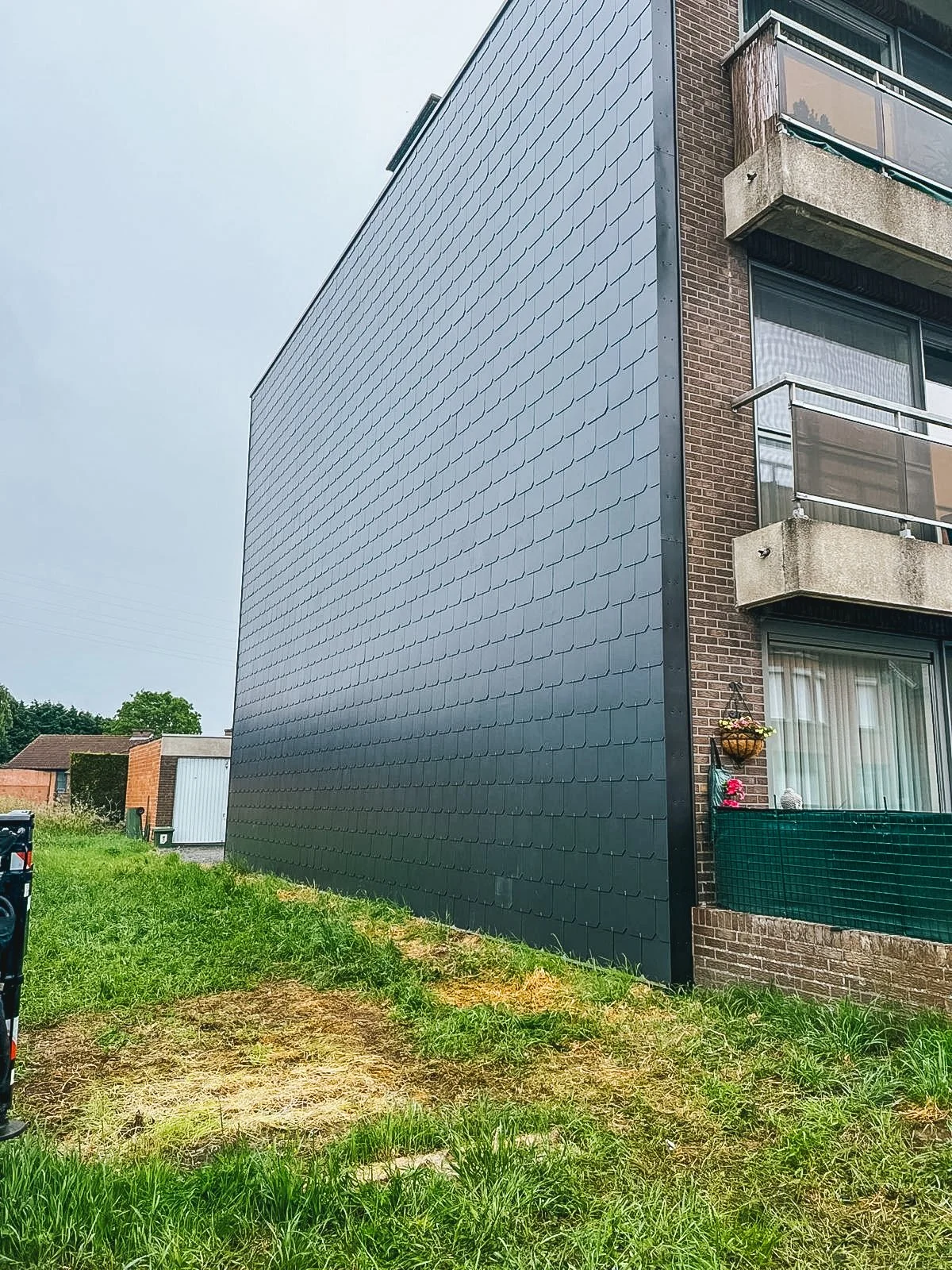 Buitengevel van een gebouw met zwarte metalen gevelbekleding aan de zijkant en balkonmetalen balustrades aan de rechterkant.