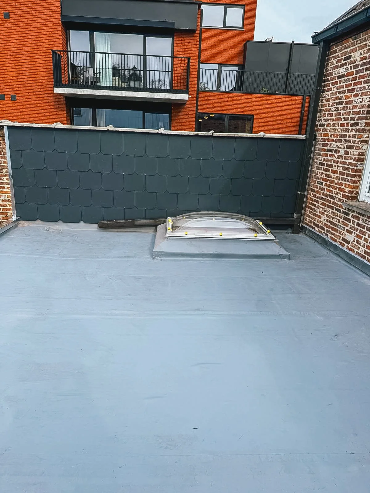 Dakterras met een bijna gladde, lichtblauwe afwerking, met een dakraam en omringd door hoge muren en moderne appartementen.